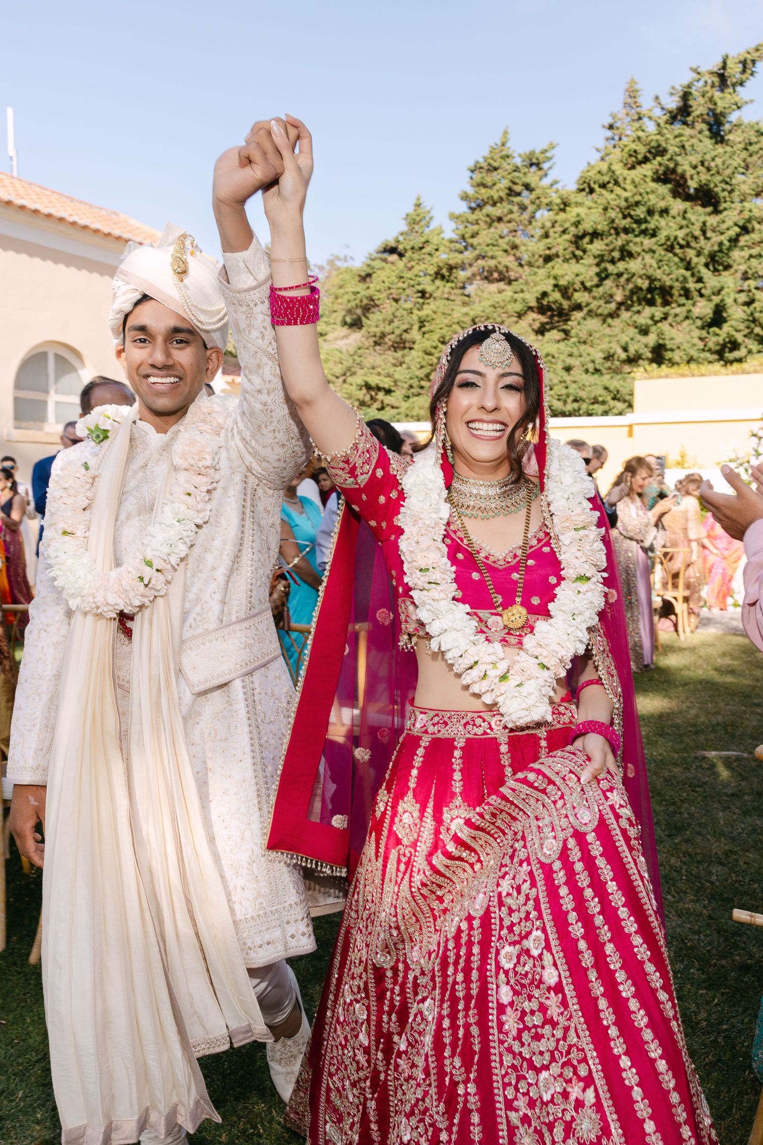 Newlyweds celebrate with raised hands wearing traditional Indian wedding garments.