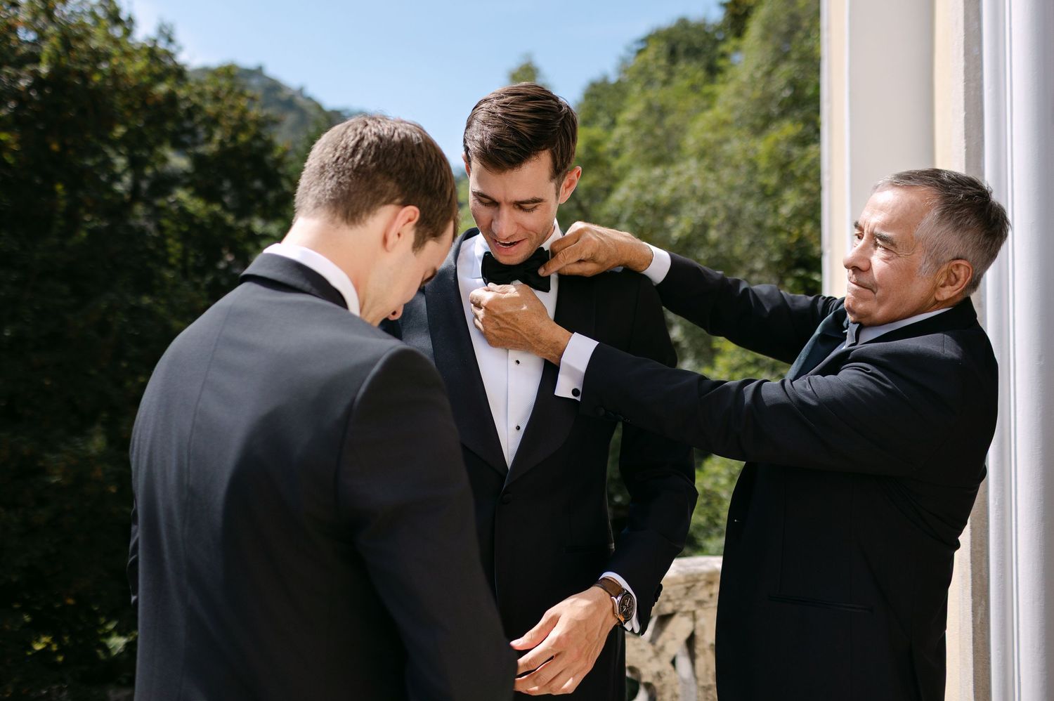 Candid moments of groomsmen helping with wedding day preparations by a window.