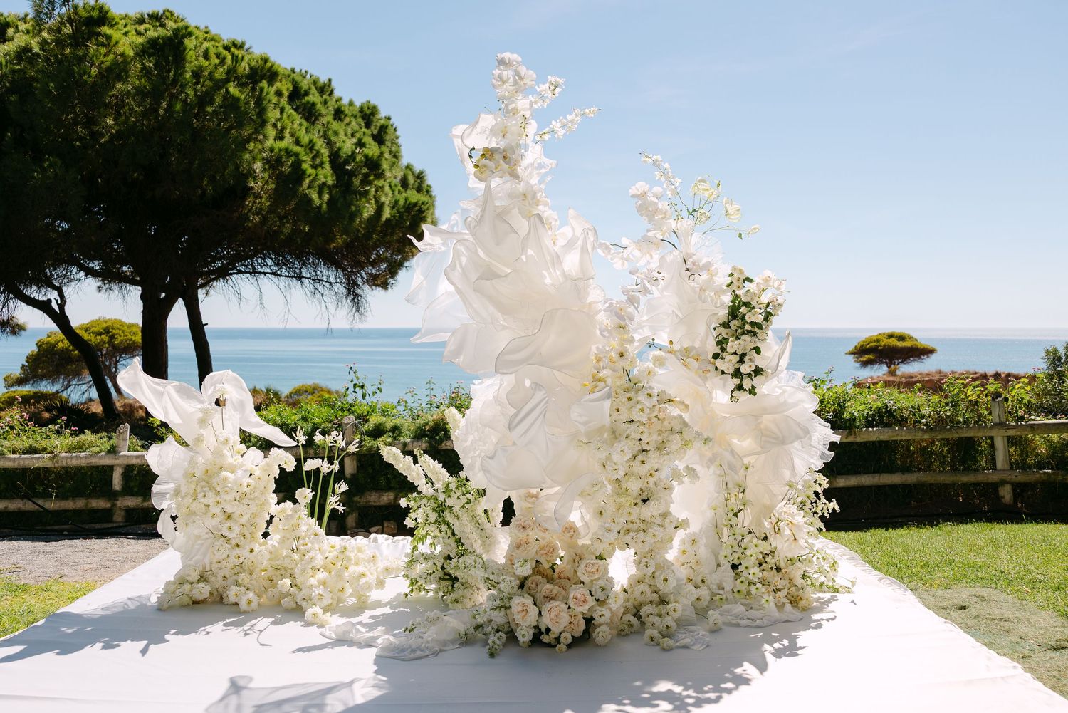 White floral arrangements and decorations adorn an outdoor wedding venue with ocean views.