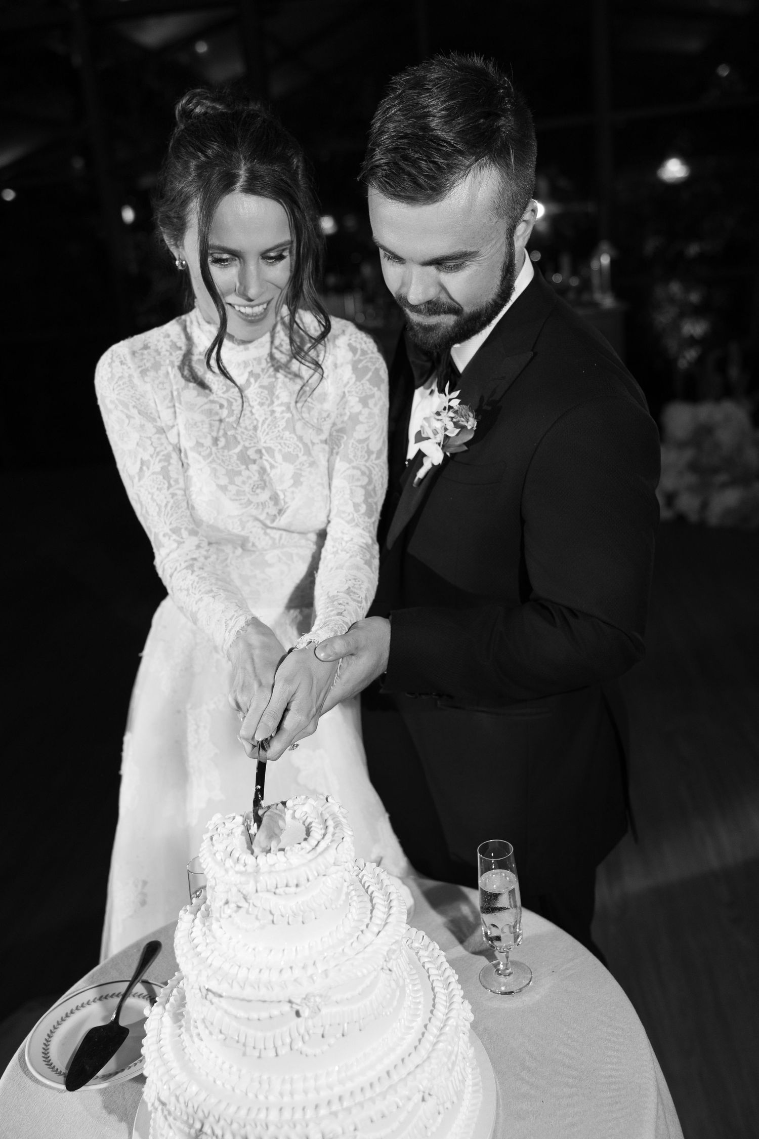 Black and white photo of couple cutting their traditional white wedding cake.