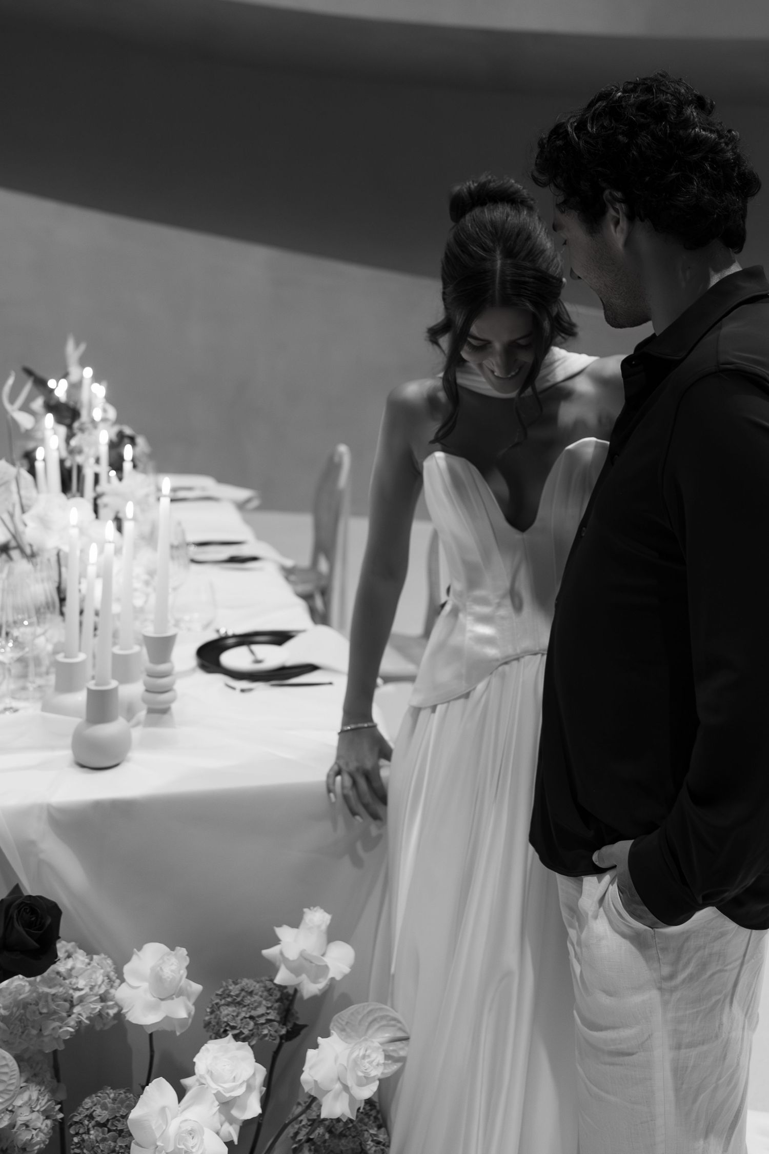 Black and white photo of a bride and groom standing together at an elegantly decorated wedding reception table.