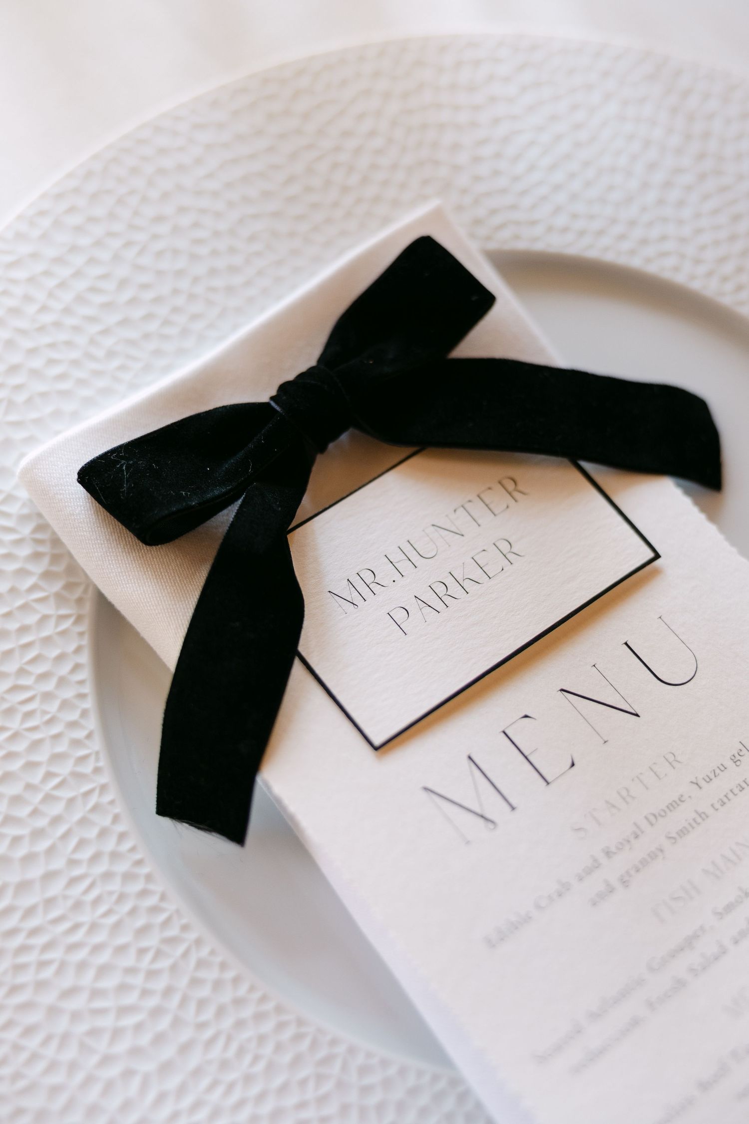 Elegant black and white wedding menu card with velvet bow on white textured plate.