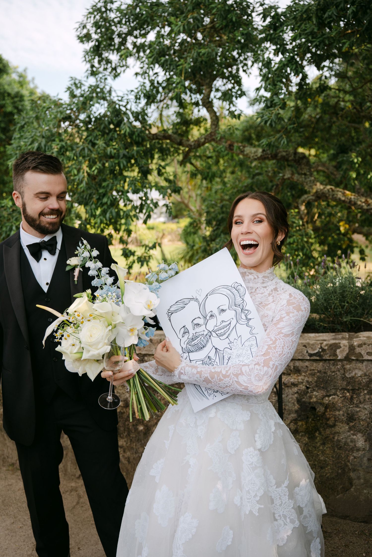 Wedding moment captured outdoors with couple sharing laughter while holding a caricature drawing.