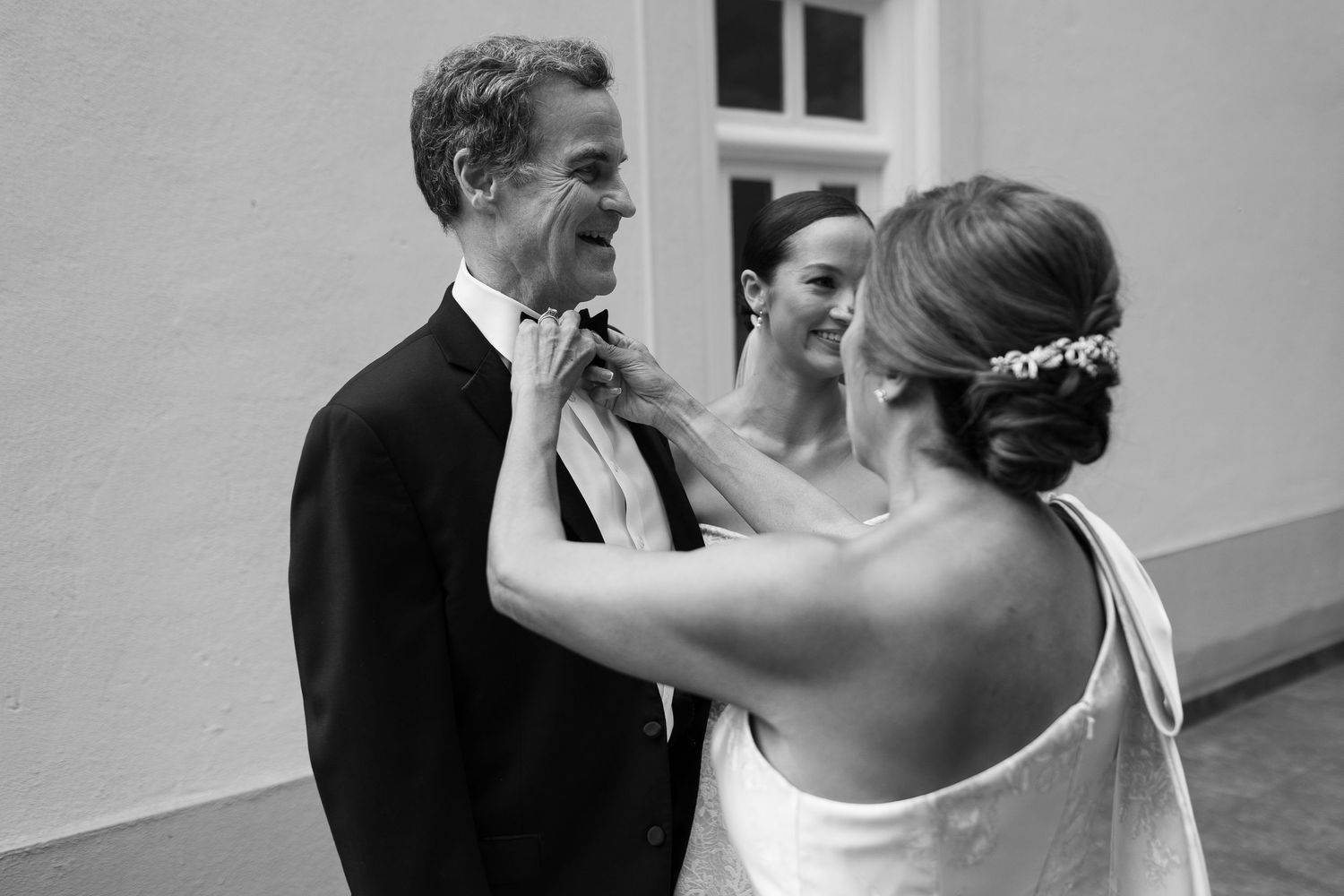 Black and white photo of wedding preparations with formal attire adjustments.