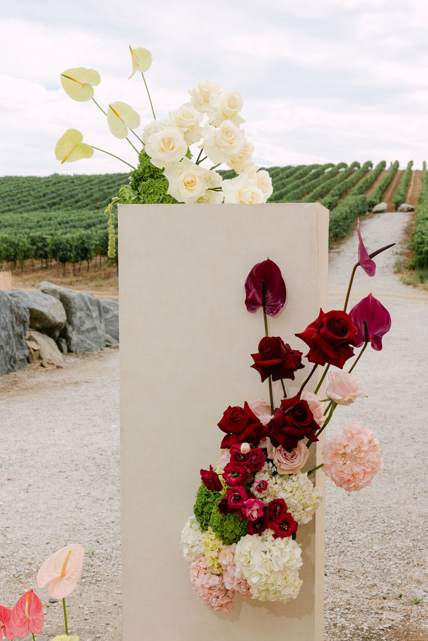 Elegant floral arrangements with deep red and pink flowers against a vineyard backdrop.