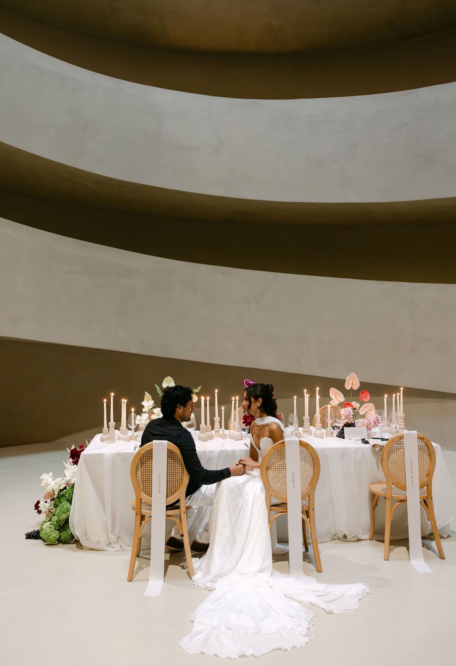 Bride and groom seated at elegant sweetheart table with candles in spiral rotunda venue.