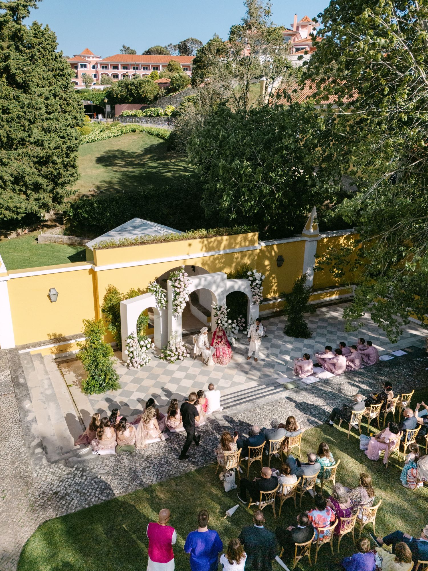 Aerial view of outdoor wedding ceremony with pink decor and seated guests.