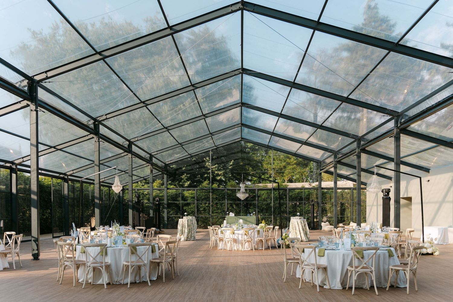 Modern glass-ceiling reception venue set up with round tables and white chairs.