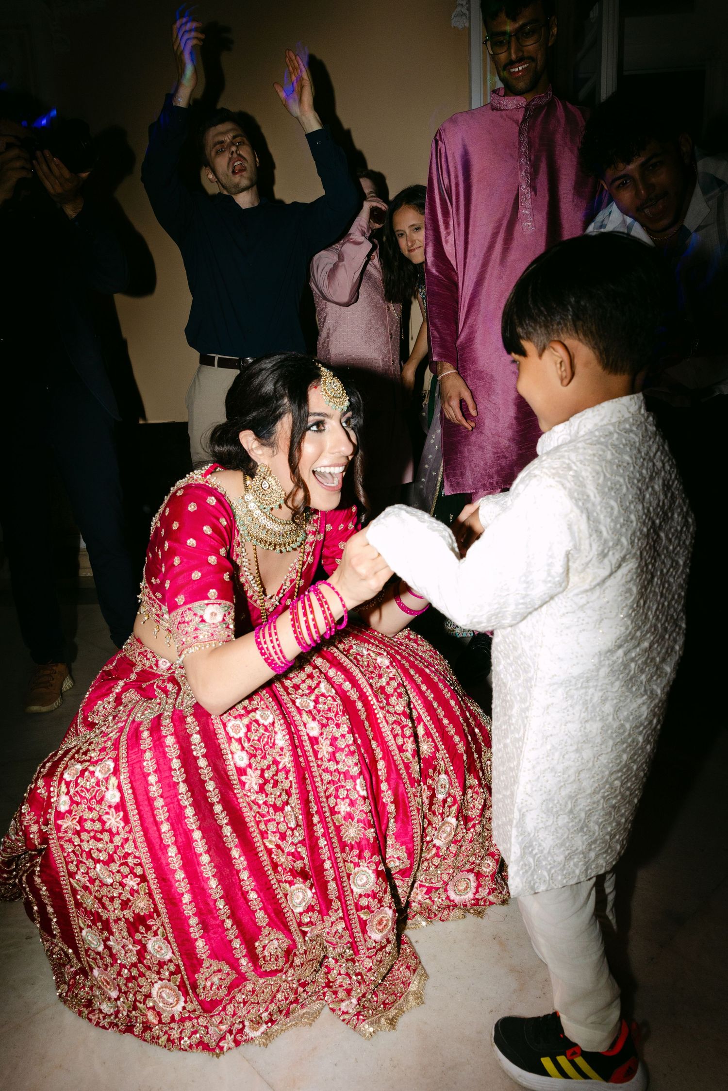 A bride in a red lehenga dances with a young guest at the wedding reception.