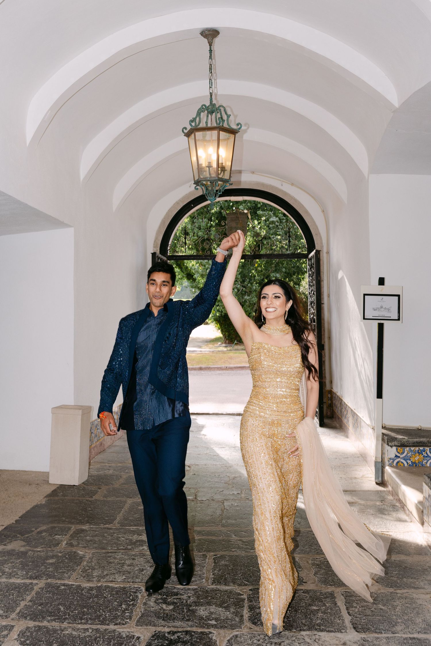 Couple in formal attire dances under arched hallway with hanging lantern.