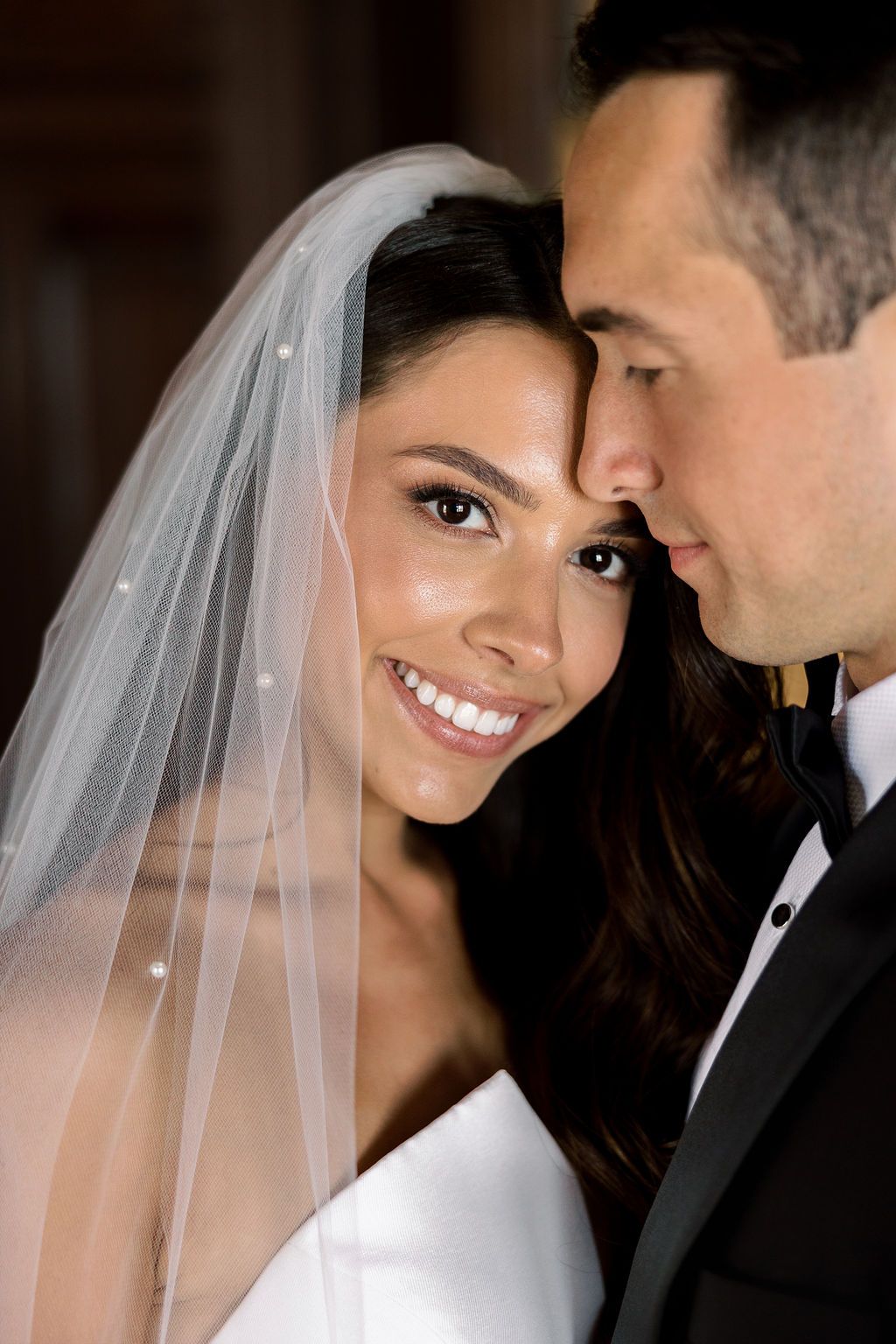 An intimate wedding portrait of a couple in formal attire with the bride wearing a traditional veil.
