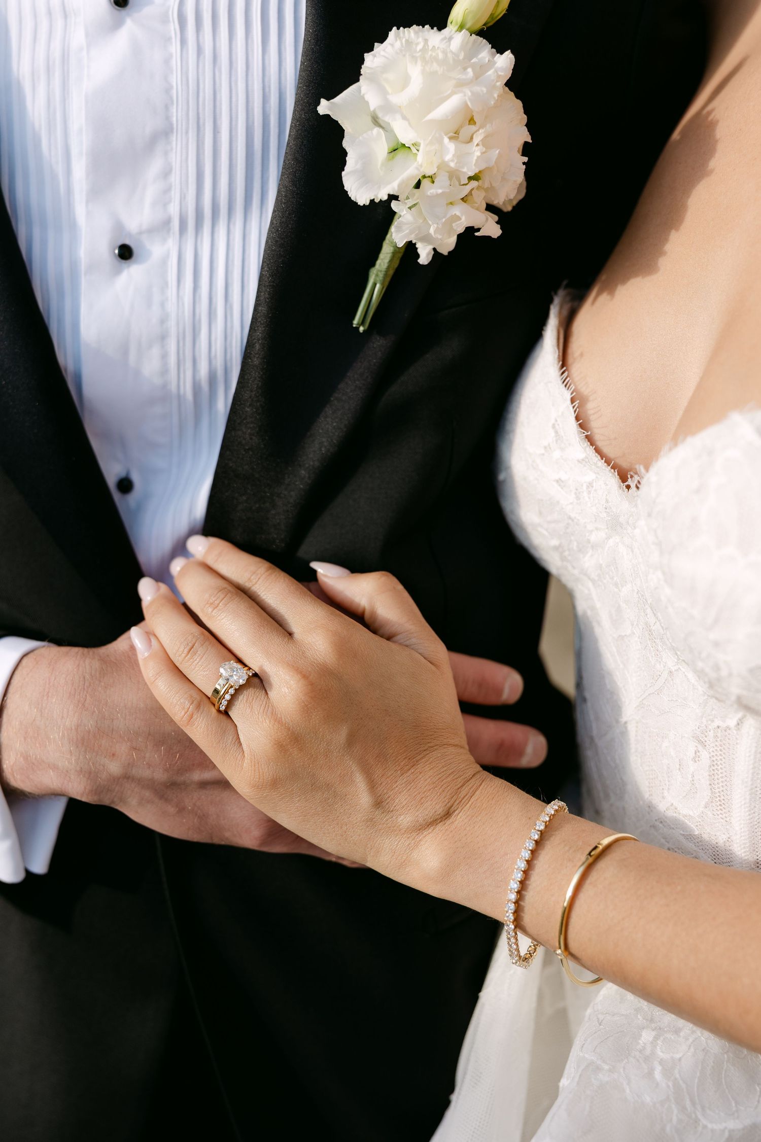 Close-up of wedding rings and white boutonniere against formal attire.