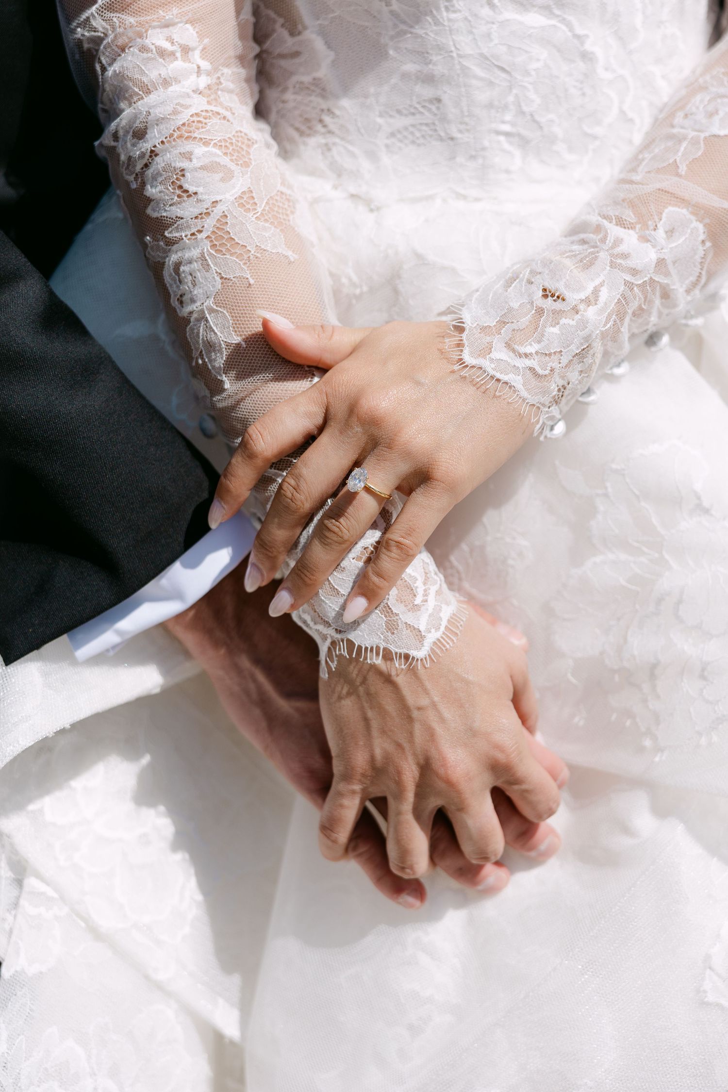 Close-up of hands wearing delicate white lace sleeves and wedding rings against a white background.