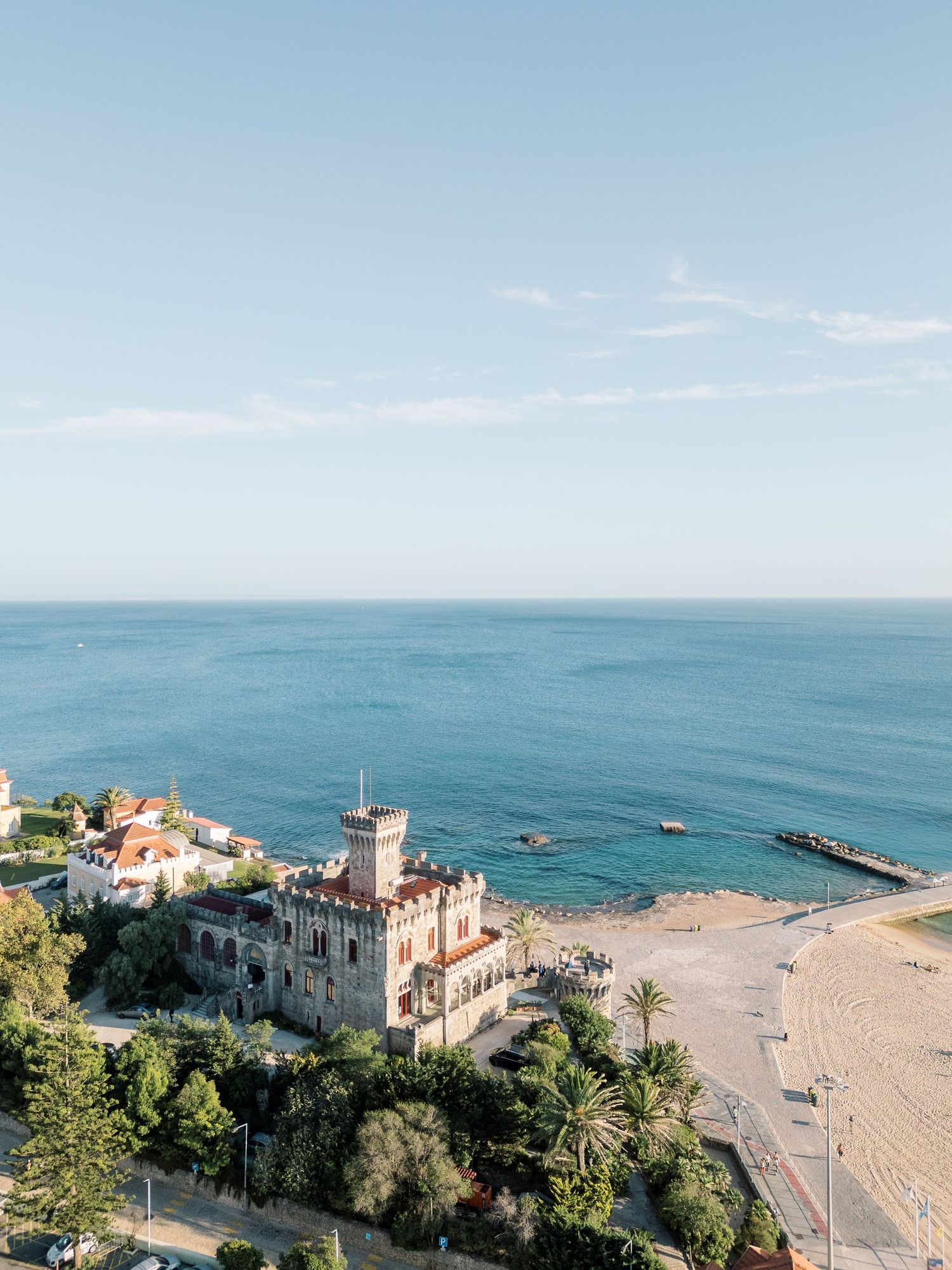 Aerial view of a coastal resort with beach, palm trees and Mediterranean architecture.