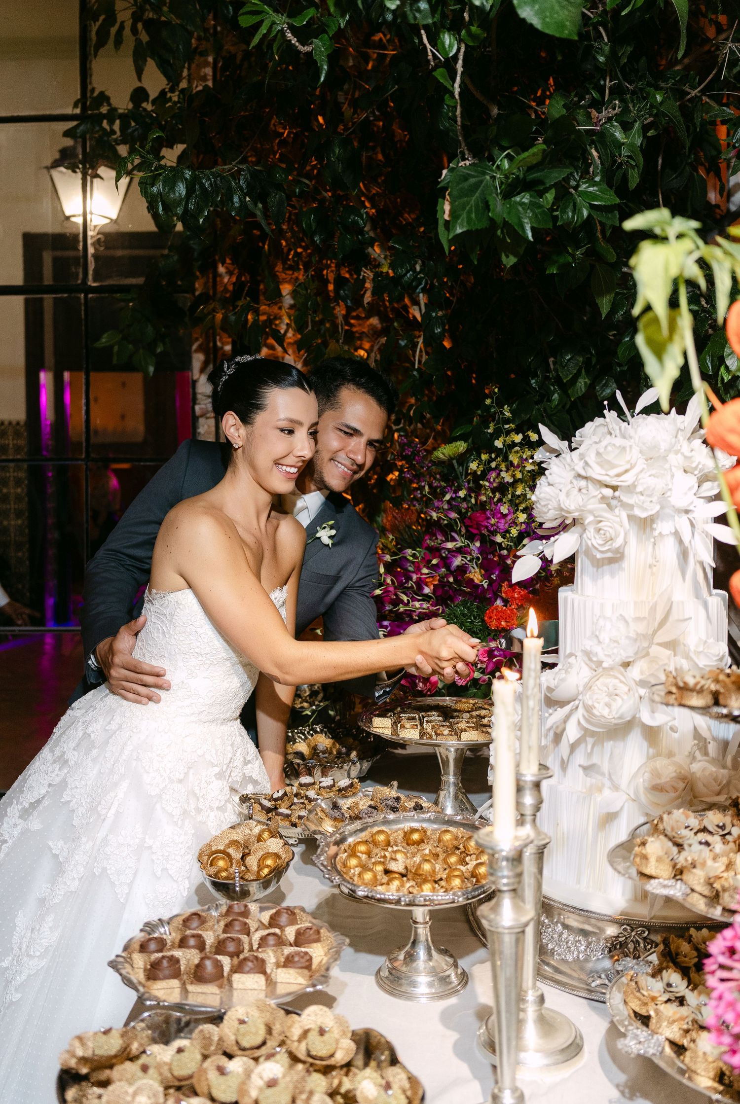 A couple examines an elegant dessert display with pastries and white decorations at their wedding.