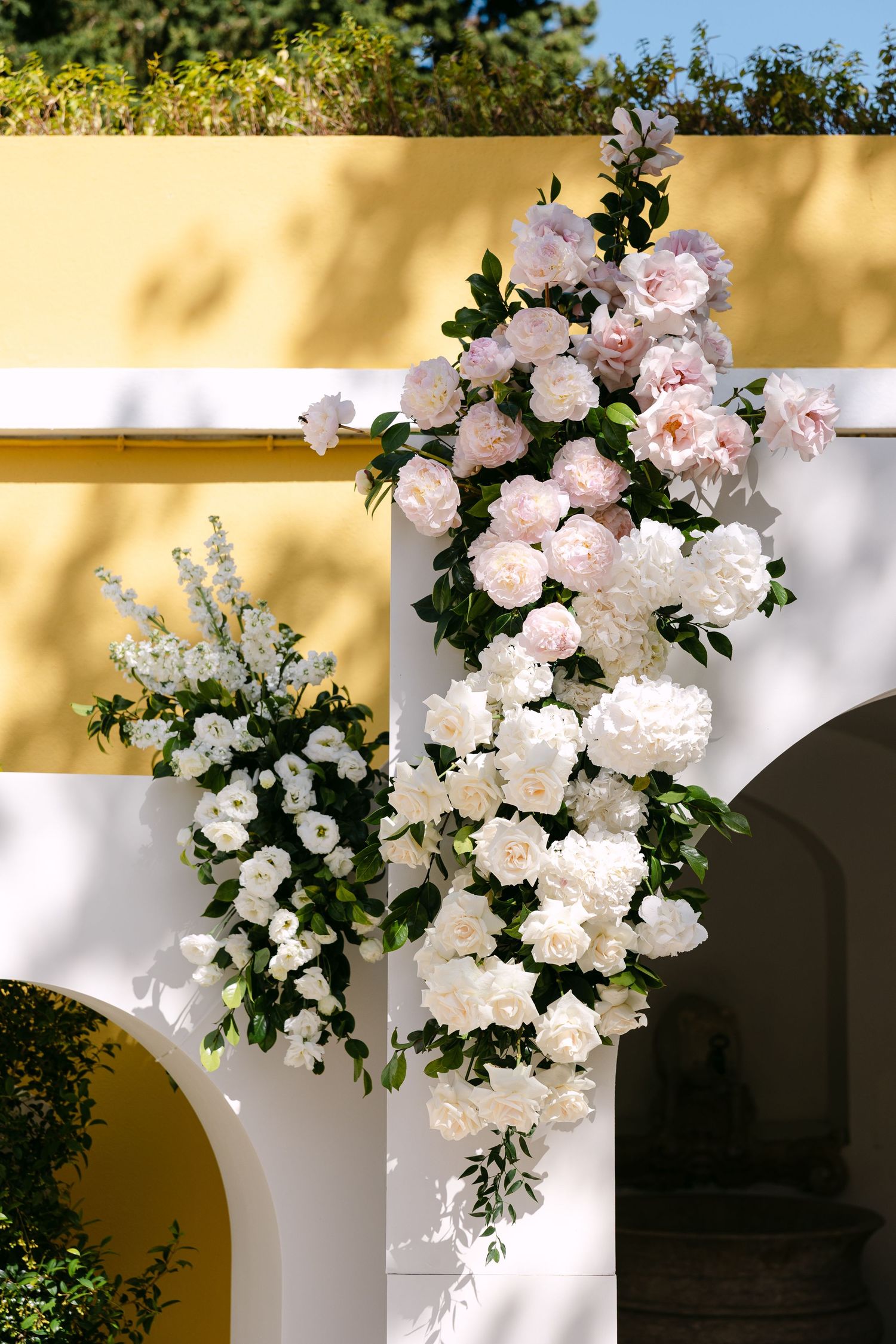 Elegant white floral arrangements with roses and greenery decorating arched walkway.