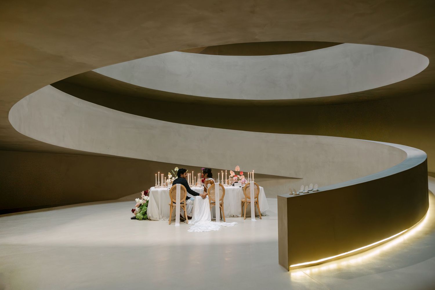 Modern architectural interior with sweeping concrete spiral curves framing an elegant wedding reception table setup.