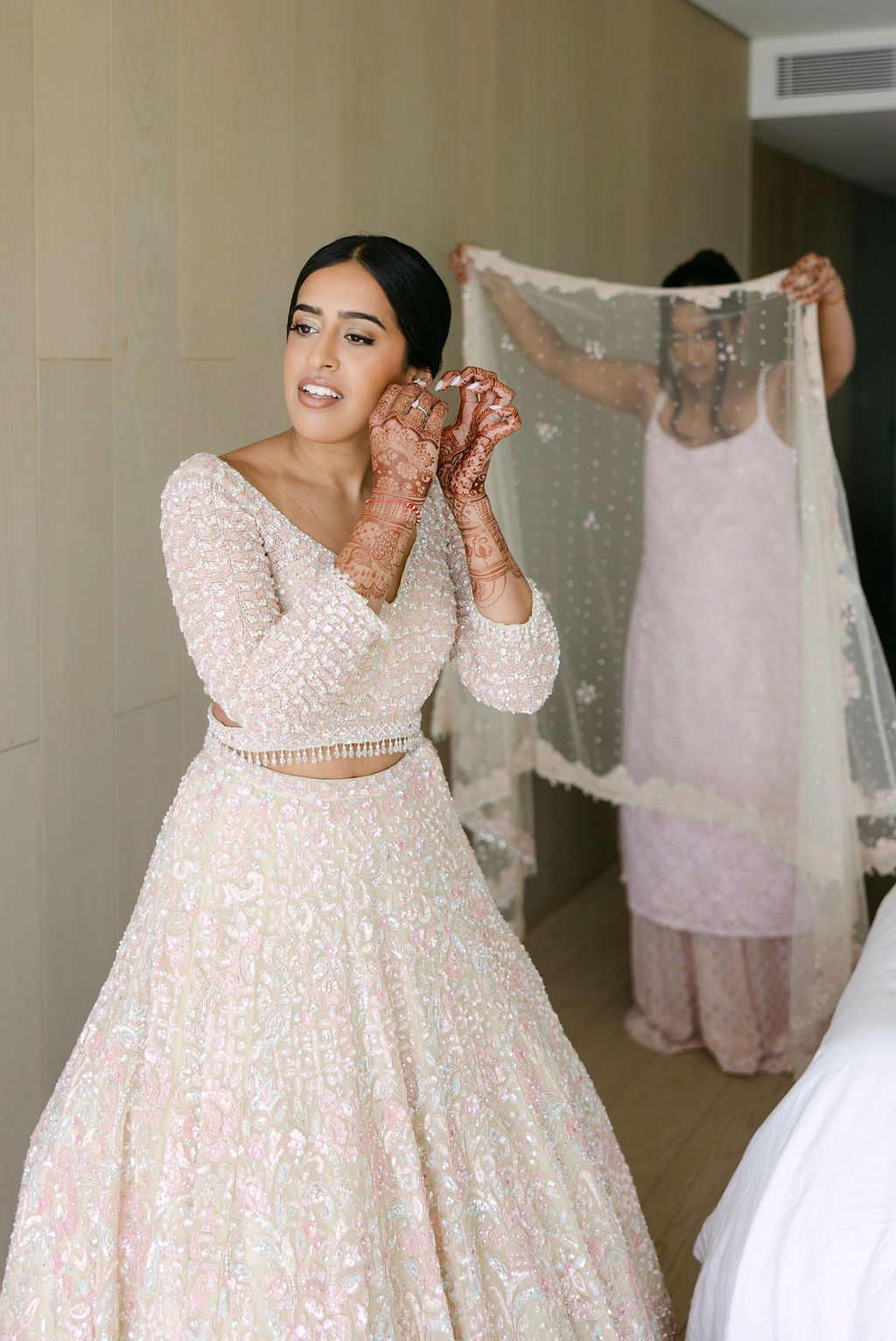 Bride in a white two-piece lehenga with long sleeves and intricate beadwork poses during wedding preparations.