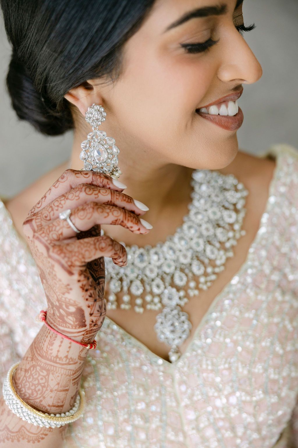 Close-up details of ornate bridal jewelry and henna-adorned hands with traditional Indian bangles.