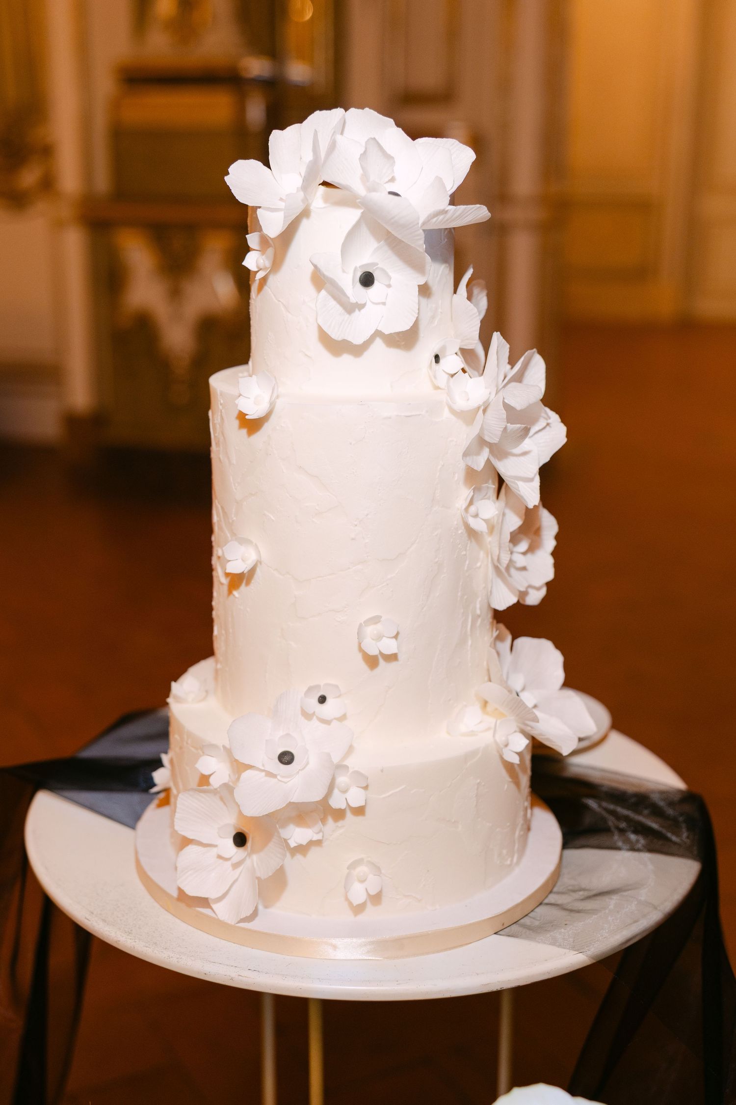 Elegant three-tier white wedding cake adorned with delicate sugar flowers on a gold stand.