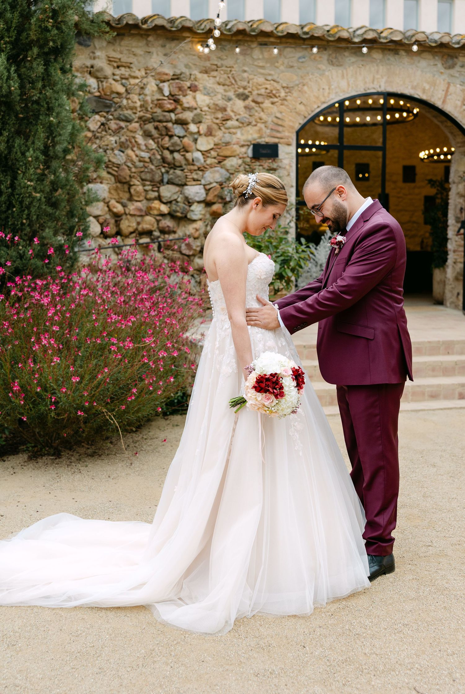 A romantic wedding moment captured in front of a stone wall with blooming pink flowers.