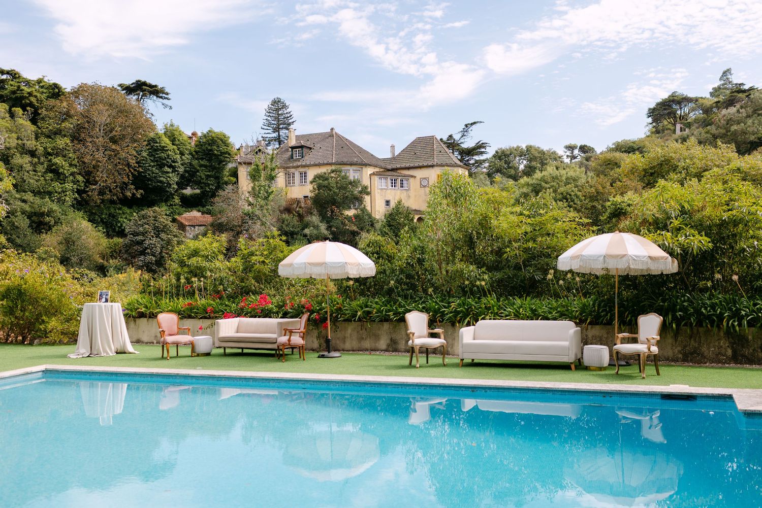 Luxury wedding venue featuring a swimming pool surrounded by manicured gardens and umbrellas.