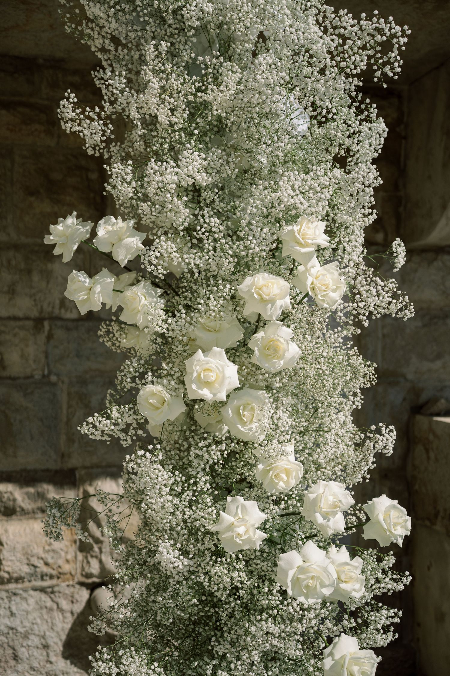 Delicate arrangement of white roses and baby's breath flowers against a dark stone background.