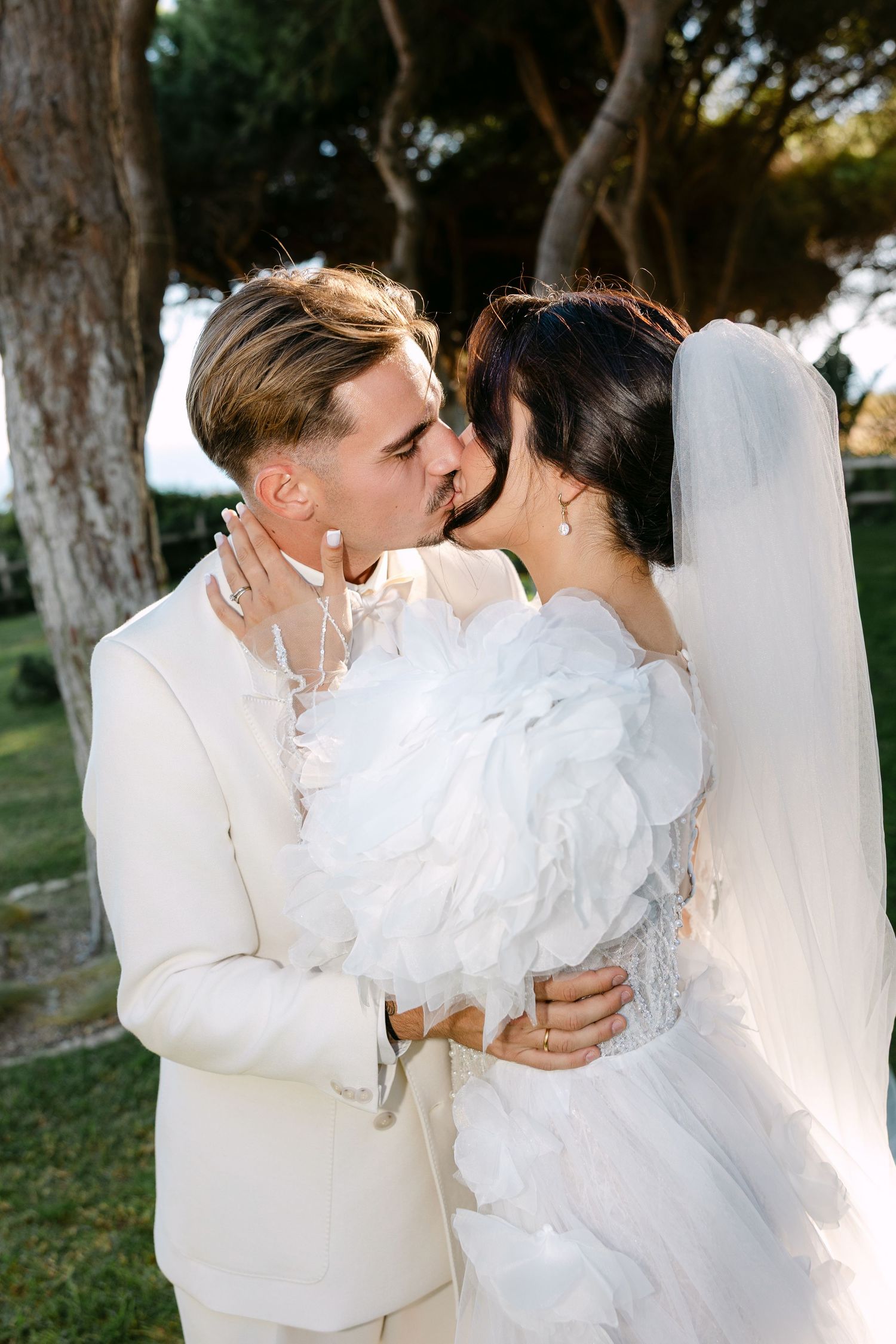 A romantic wedding moment captured outdoors under tall trees.