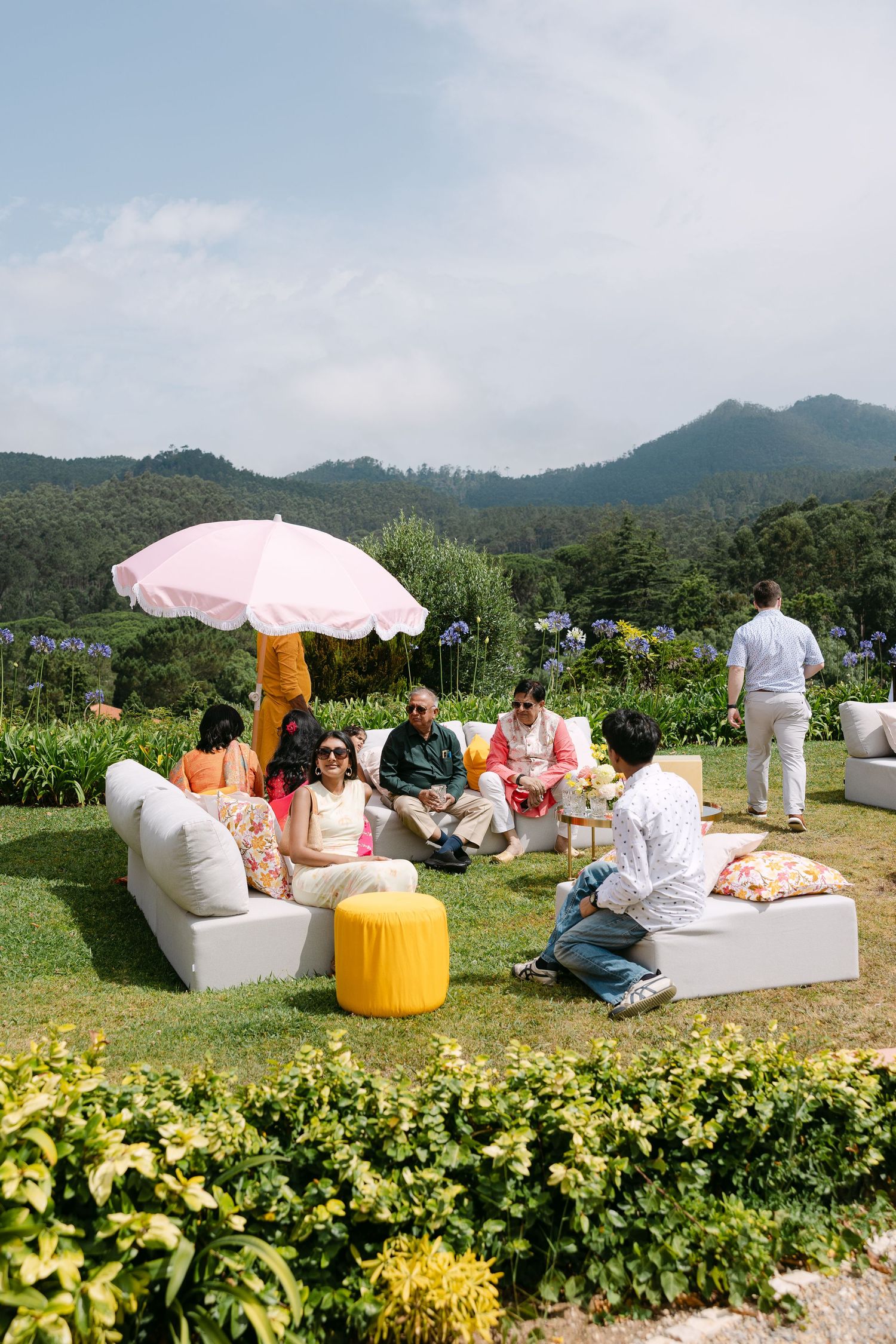Outdoor lounge area with white couches and umbrellas set up on a grassy hill with mountain views.