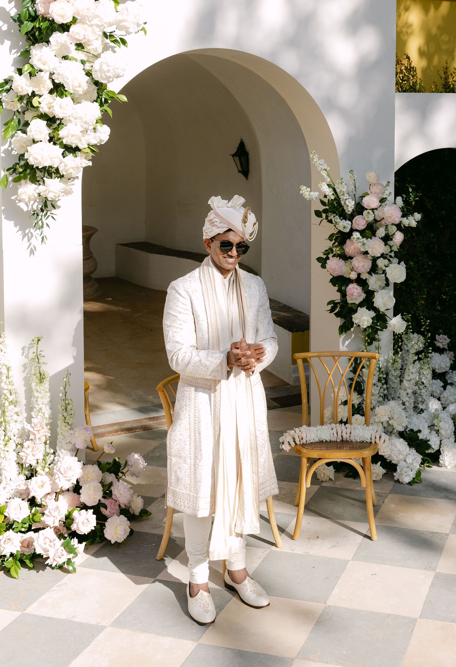 Traditional wedding attire against white archway decorated with elegant white flowers.