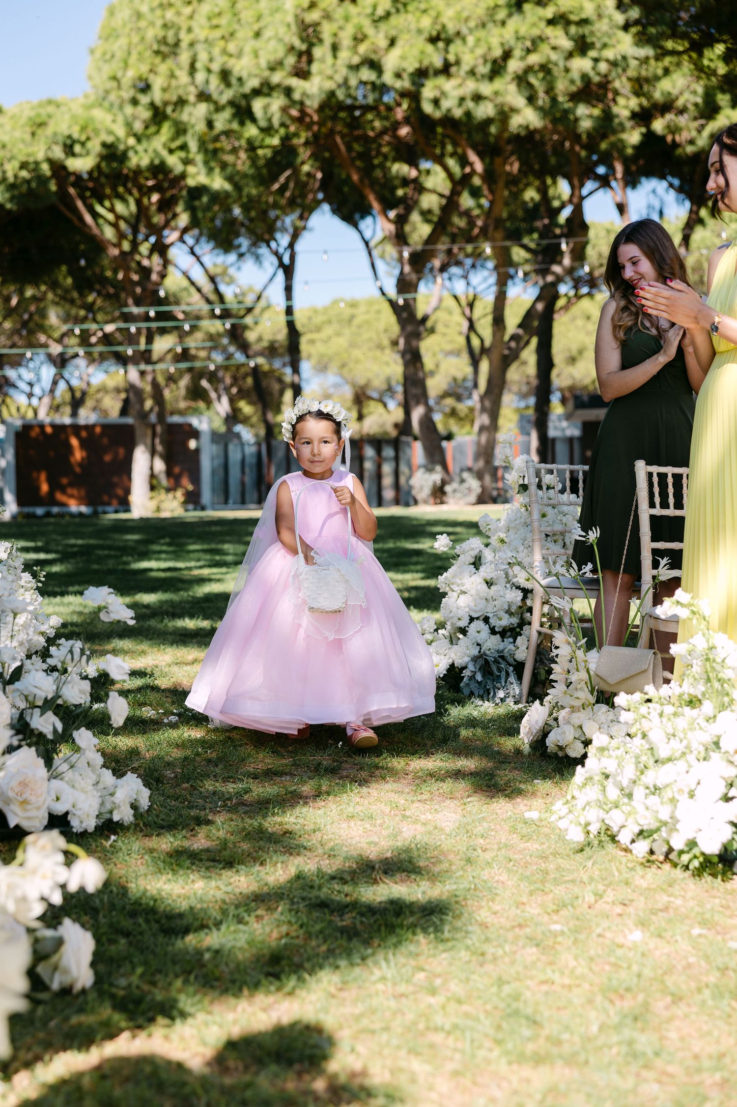 Outdoor garden wedding scene with white floral decorations and pink accents.