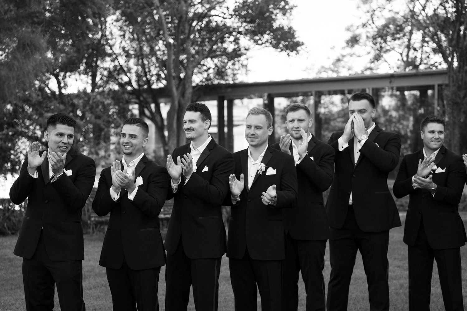 Wedding party in black formal attire poses for group photos outdoors.
