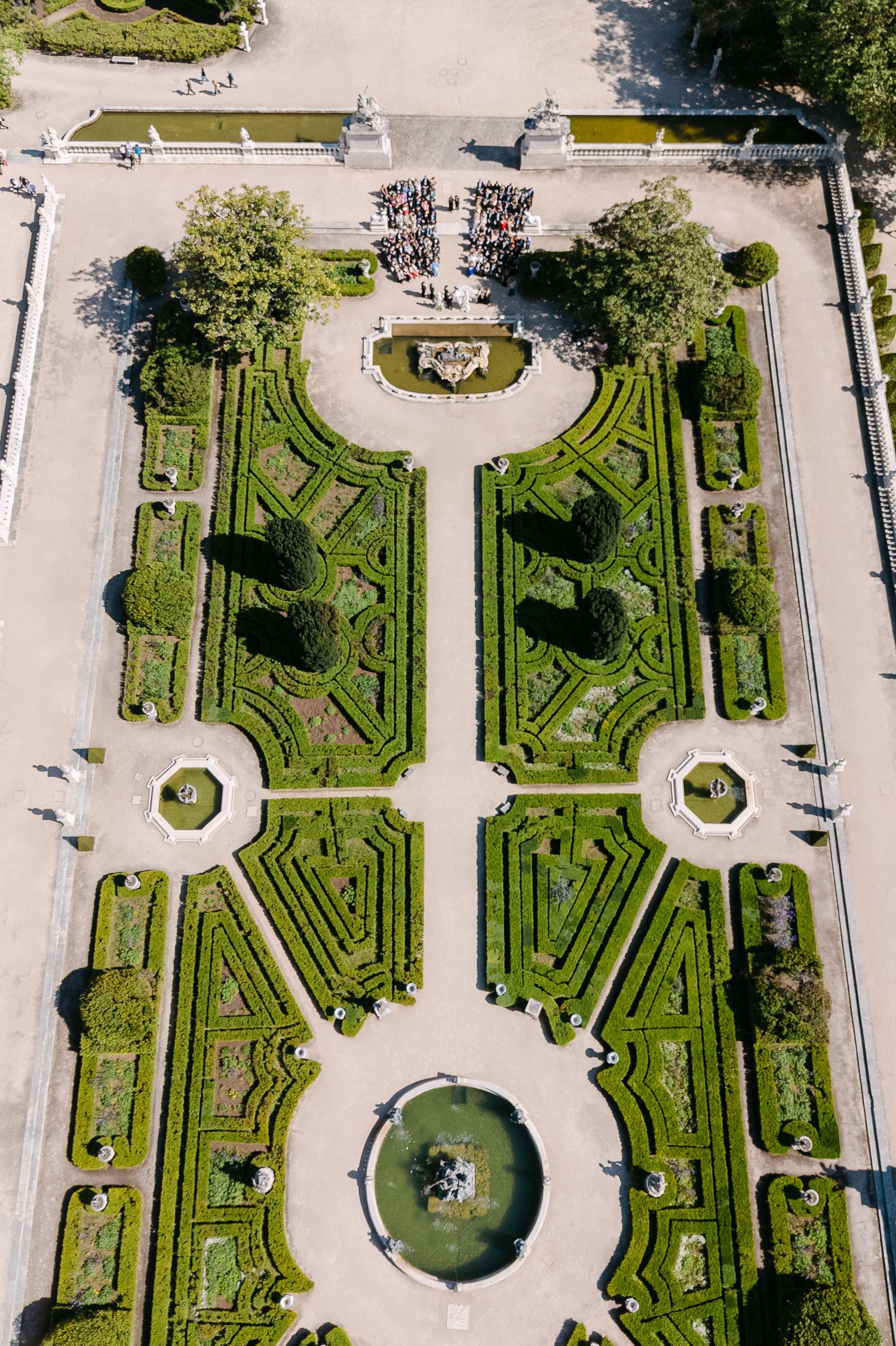 Aerial view of a formal symmetrical garden with geometric hedges, pathways, and fountains at a grand estate.