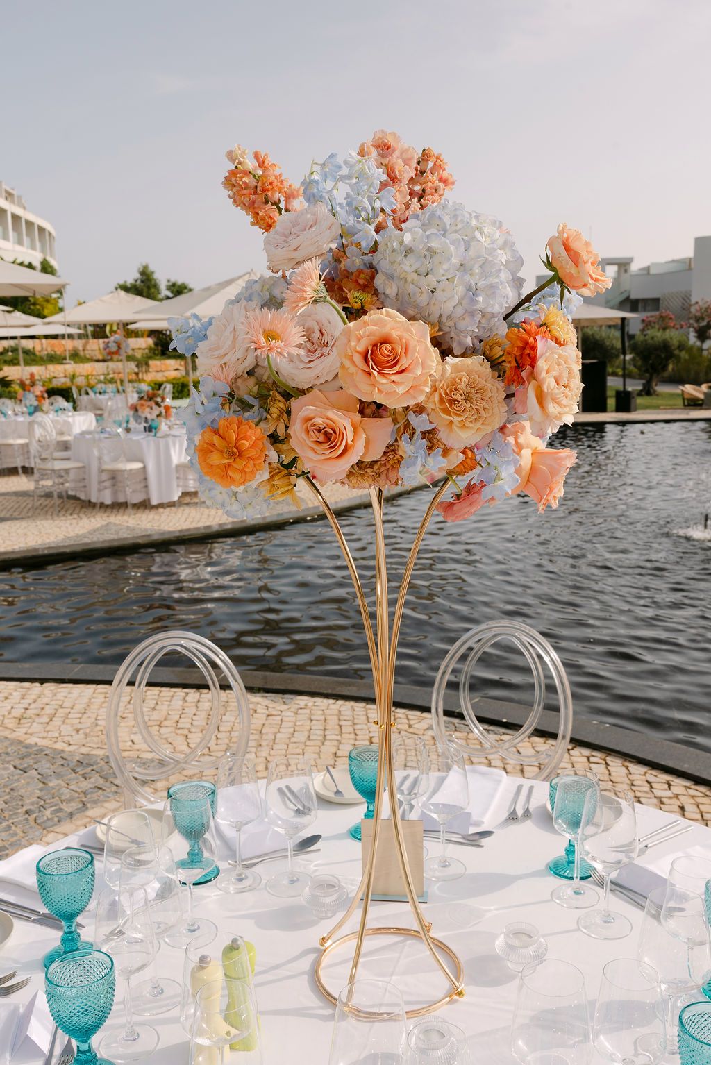 Elegant table setting with peach floral centerpieces and turquoise glassware by waterfront.