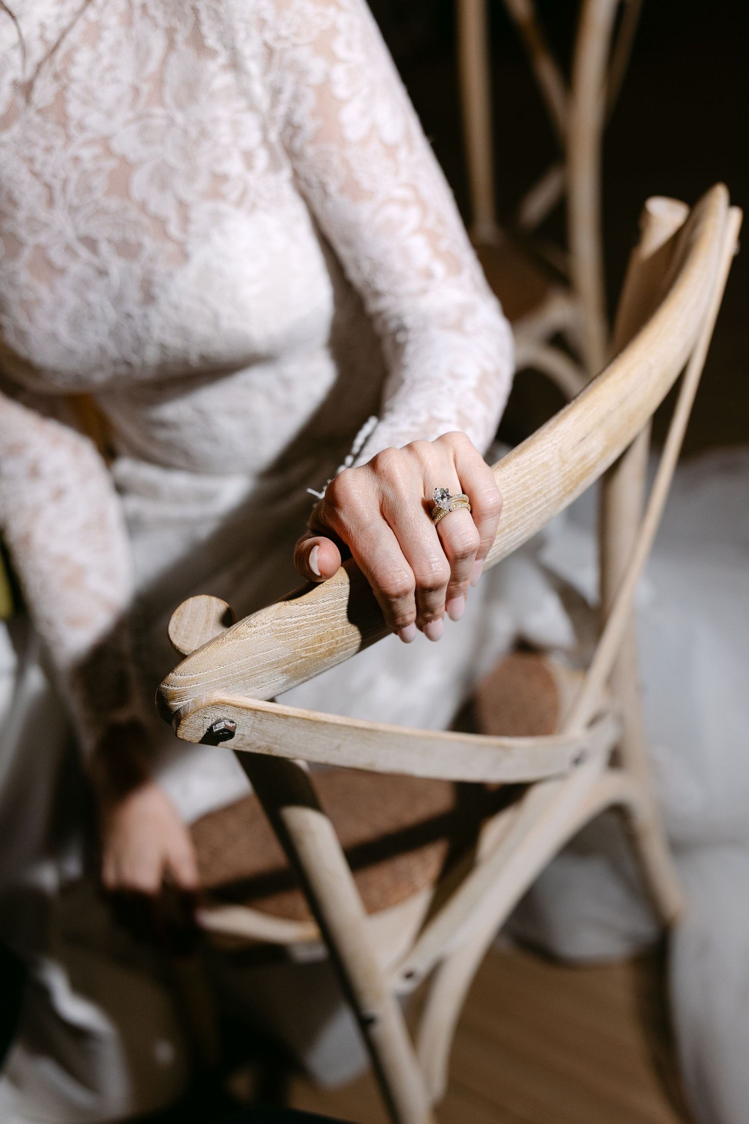 Close-up details of white lace wedding dress and hands adjusting shoes.