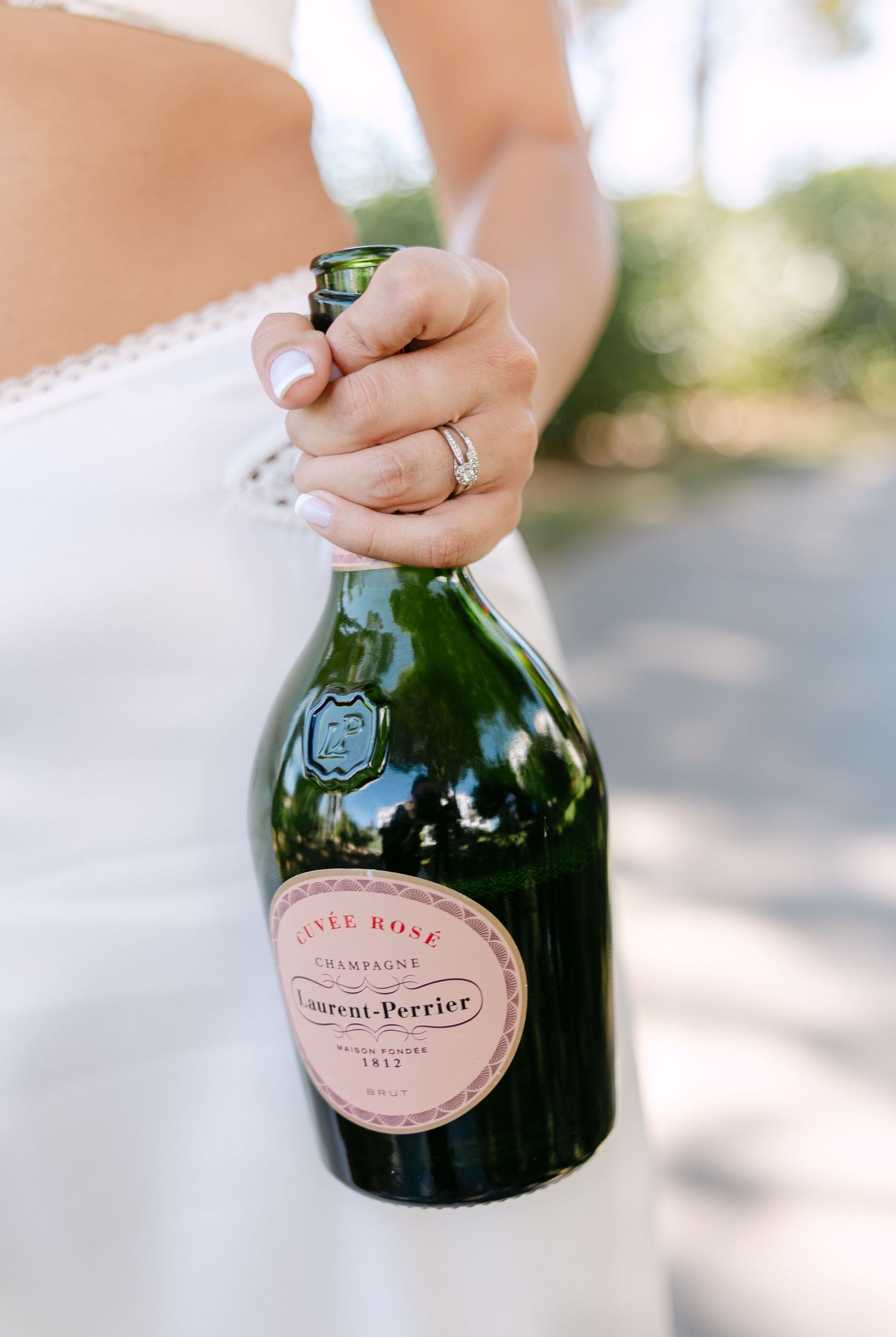Champagne bottles with pink labels being held in natural outdoor lighting.