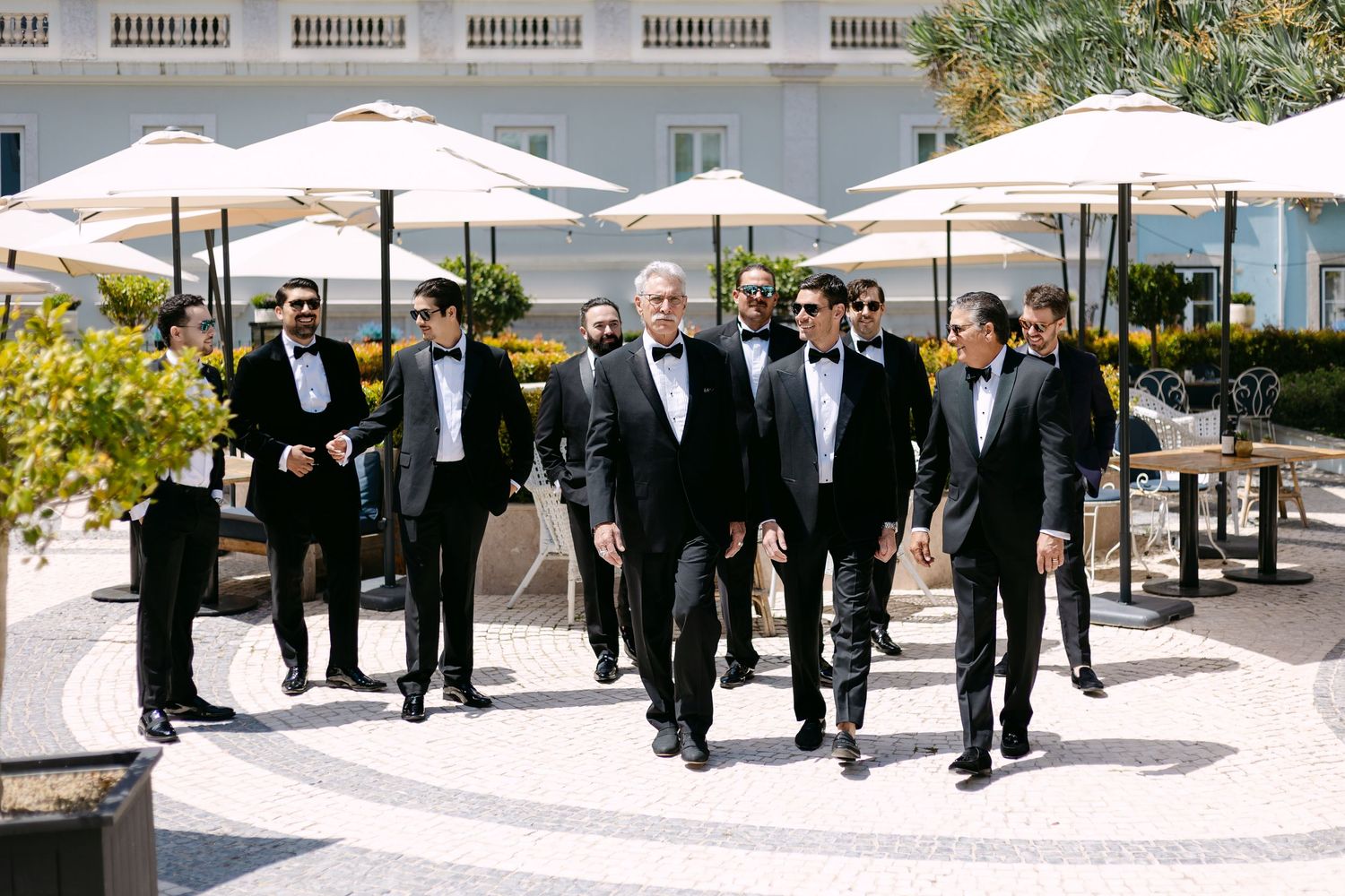 Wedding party walking outdoors under white umbrellas in a line formation.