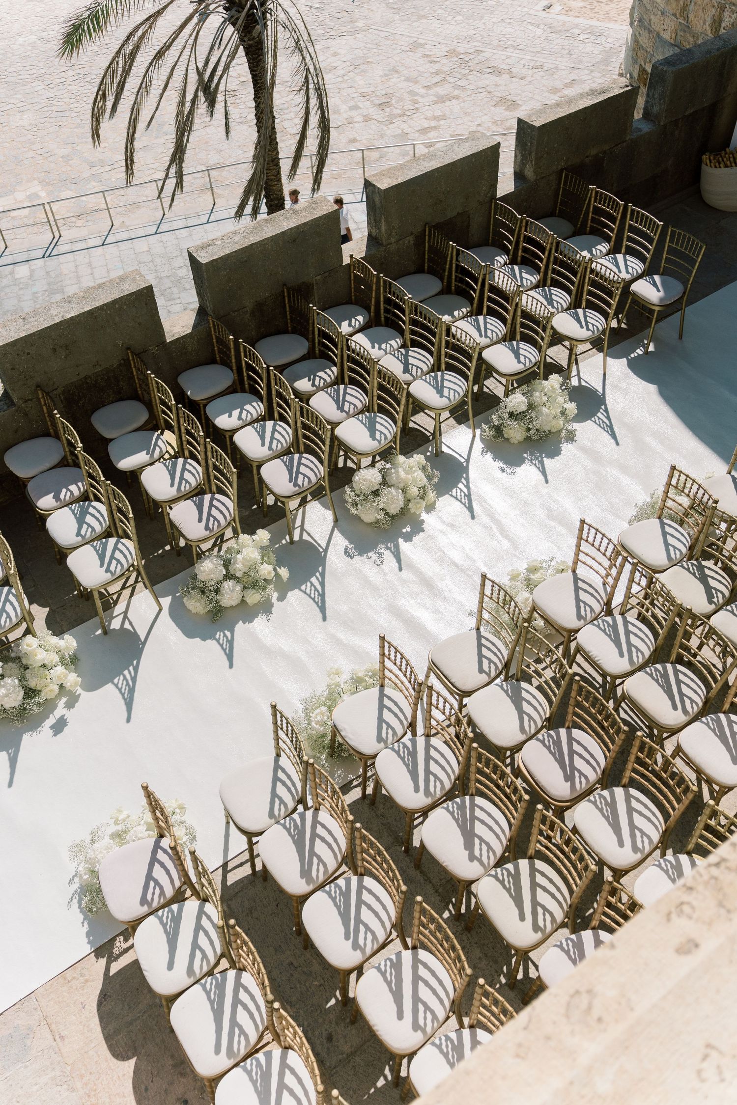 Rows of elegant gold chiavari chairs arranged outdoors for a wedding ceremony with palm trees in the background.