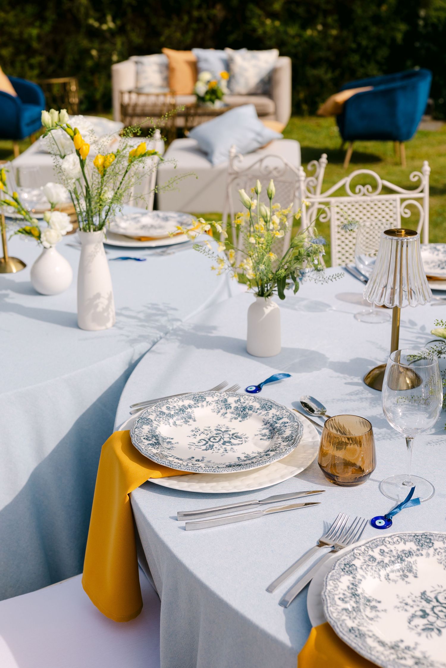 Elegant table setting with blue and white china plates, yellow napkins, and wildflower centerpieces.