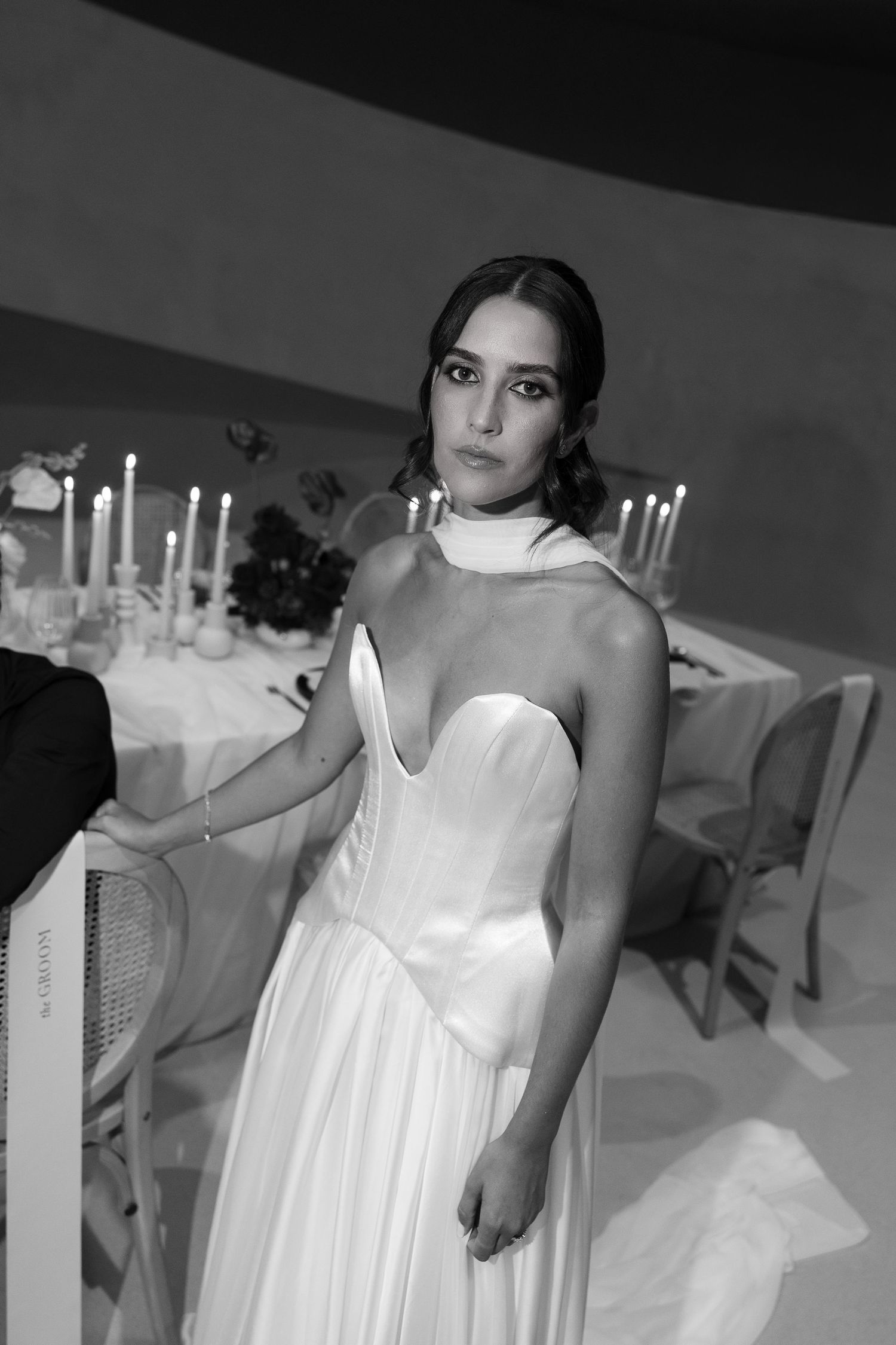 Bride in strapless white gown with halter neckline poses by candlelit reception table.