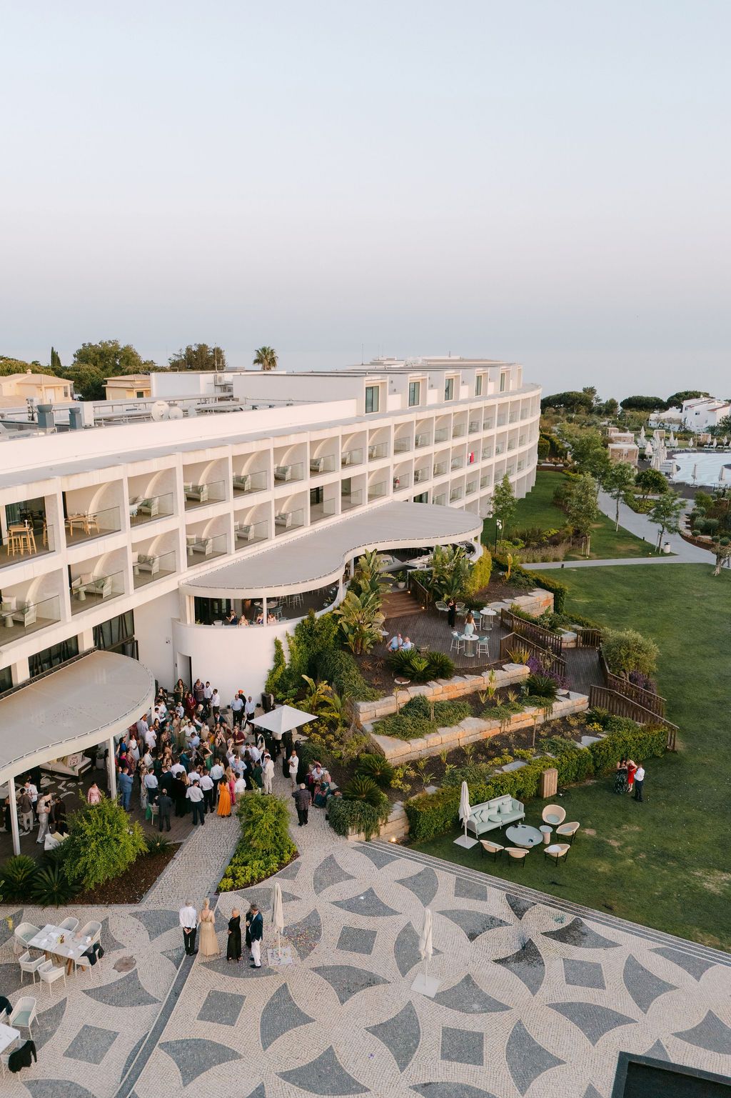 Modern white architectural venue with outdoor terrace and gathering spaces overlooking landscaped grounds.