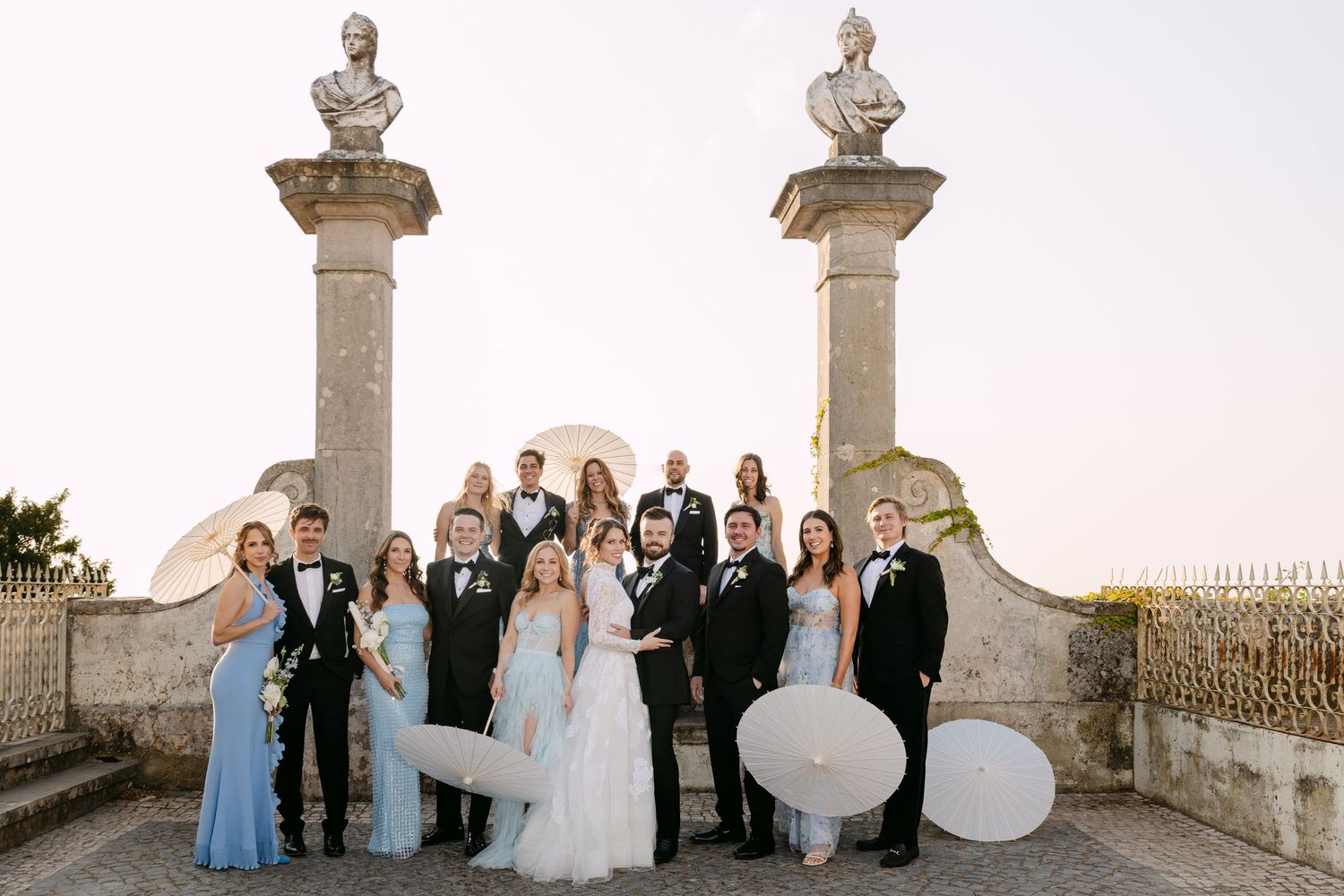 Wedding party posing with large balloon letters on an ornate stone terrace.