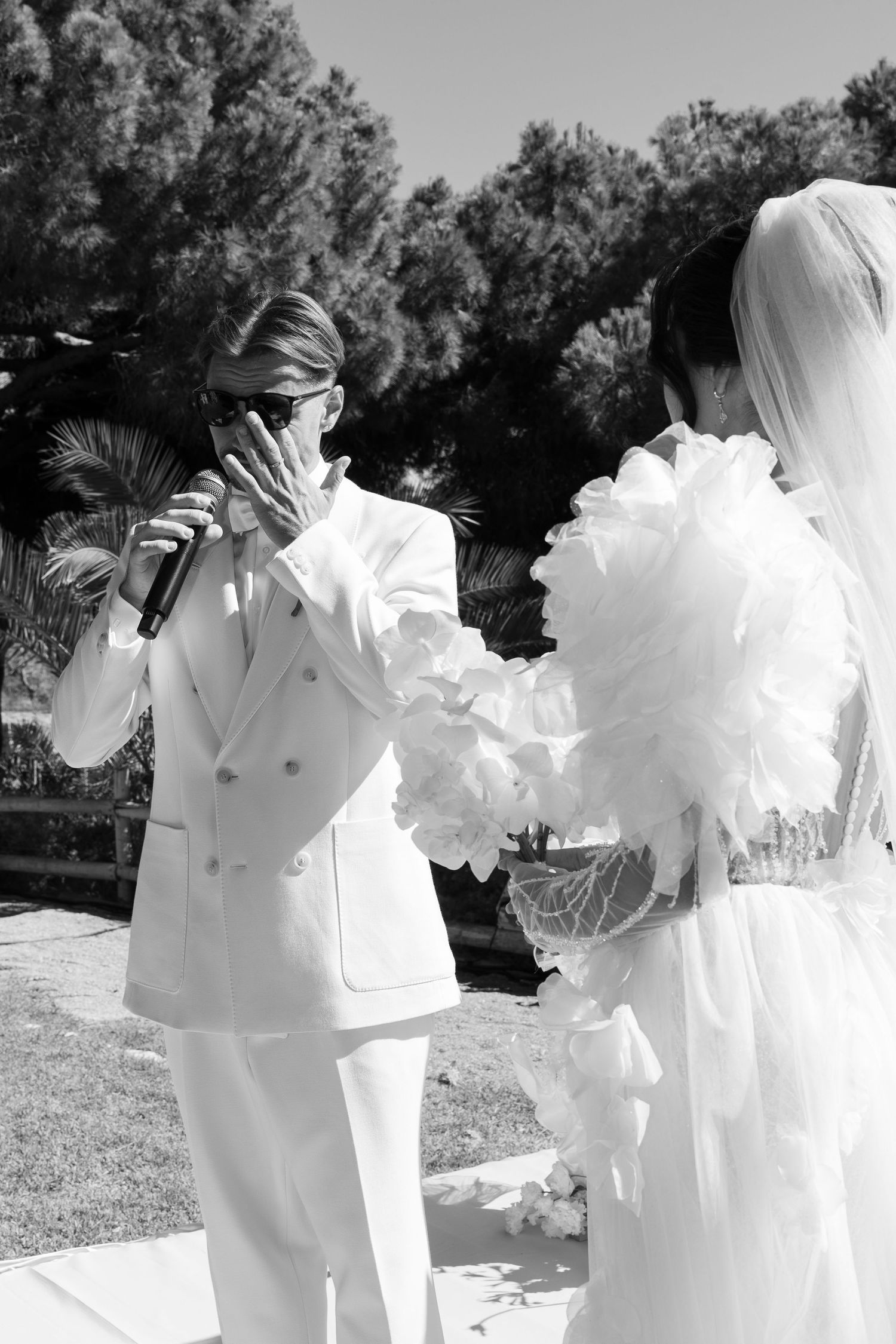 A wedding ceremony moment captured in black and white showing formal attire and a microphone.
