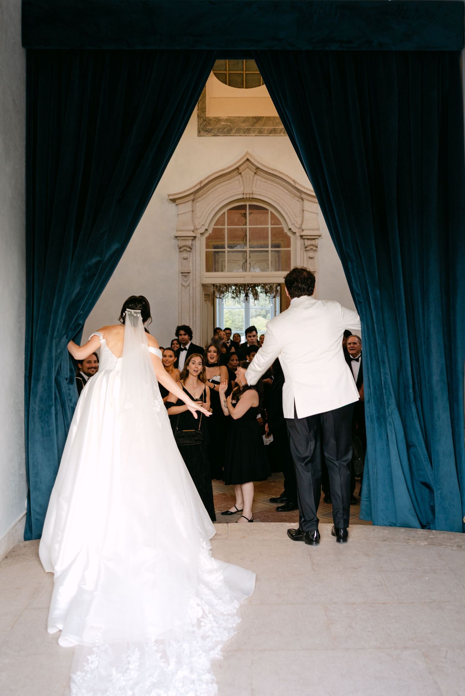 Wedding party poses behind blue curtains in an elegant white interior space.