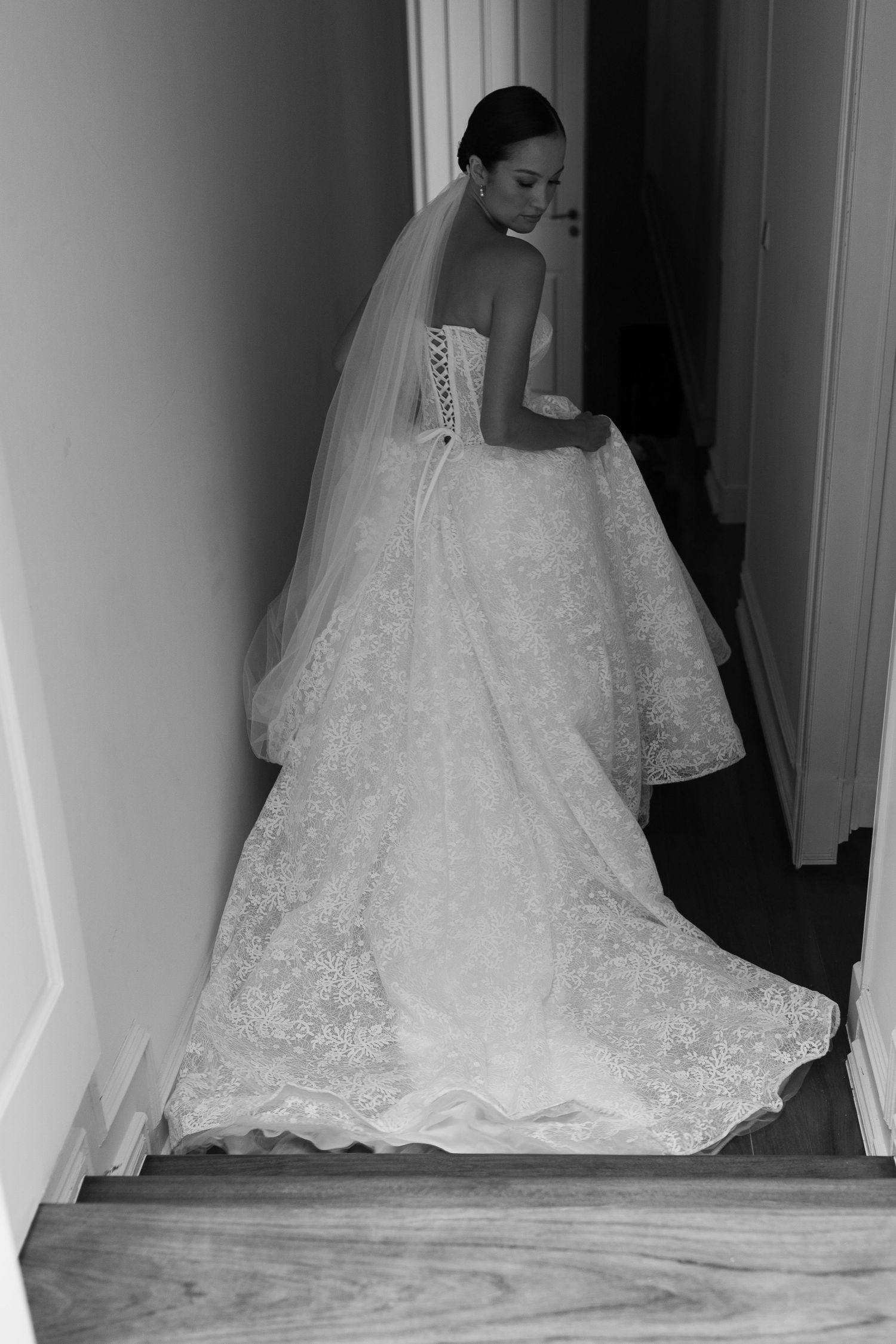 Black and white photo of wedding dress with lace train on wooden staircase.