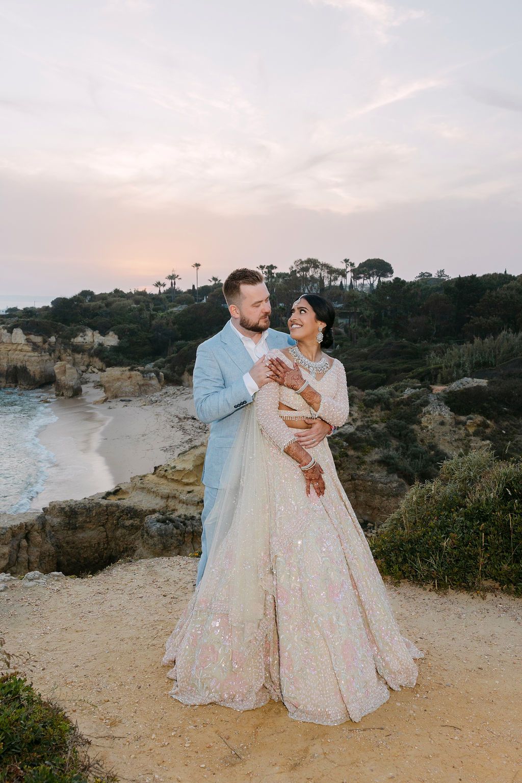 Couple embracing on a scenic coastal cliff during golden hour.