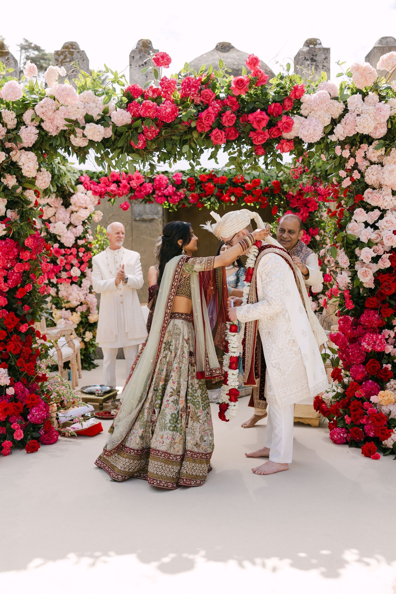 Wedding ceremony setup with lush pink and red rose archways and decorative floral arrangements.
