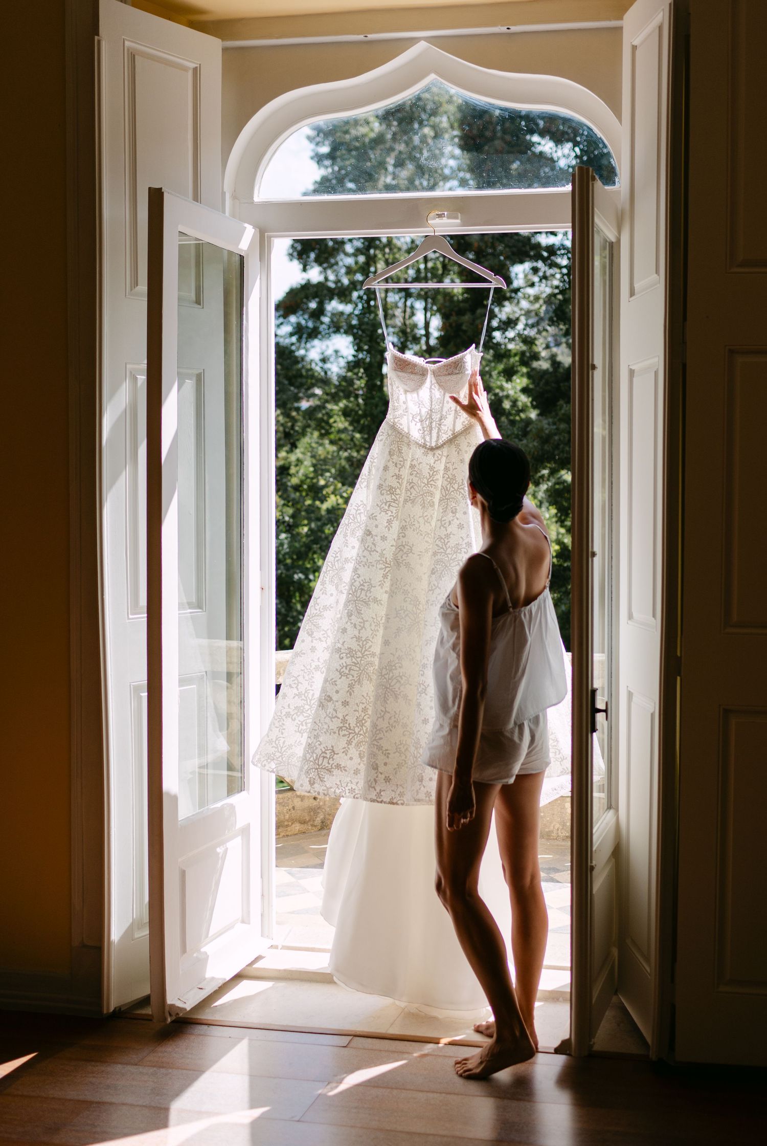 Beautiful white wedding dress displayed in an elegant room with arched windows and natural light.