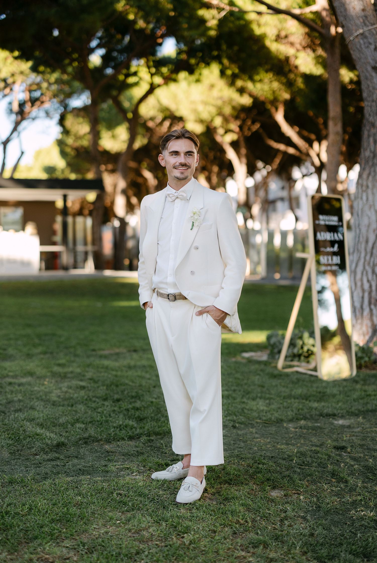 A person in an all-white suit poses confidently on a grassy lawn.