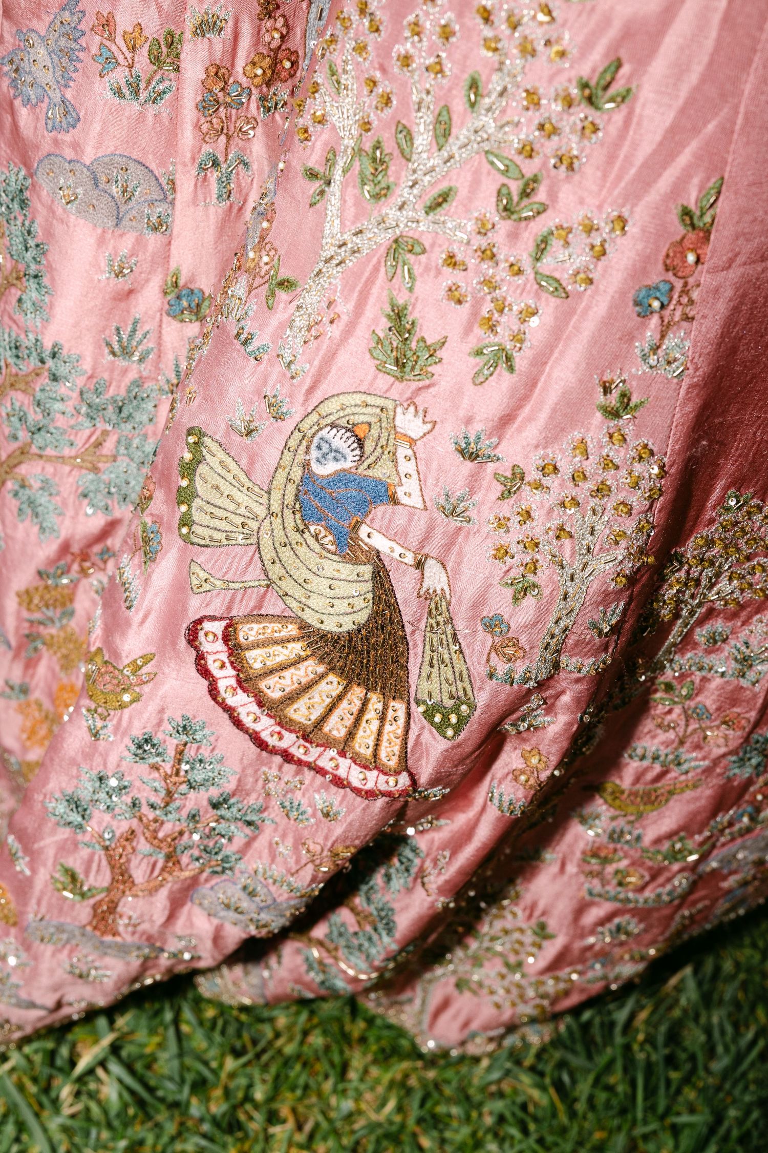 Detailed embroidery of peacock on pink fabric with floral designs.